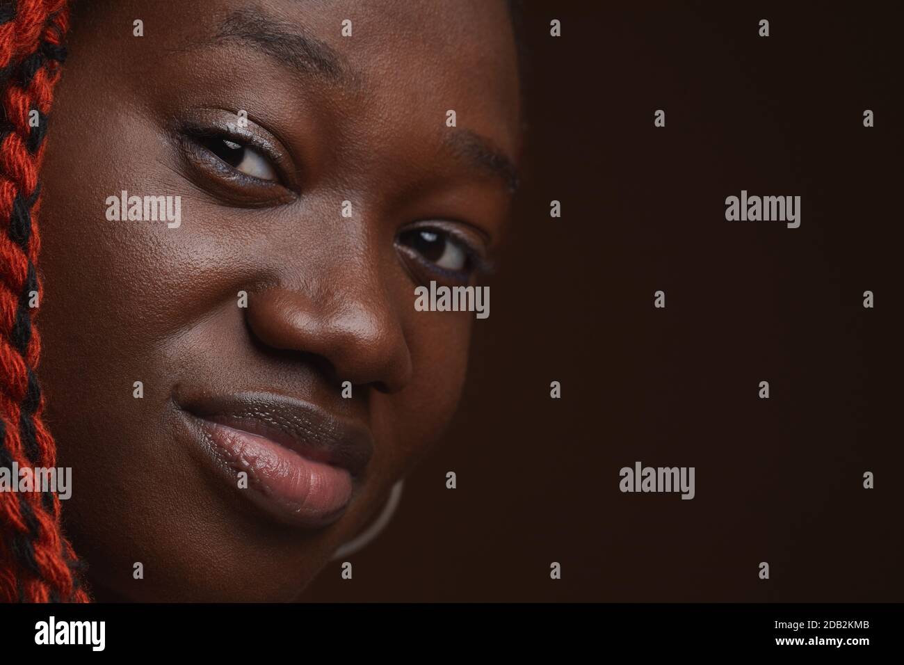 Extreme Nahaufnahme Porträt einer jungen afroamerikanischen Frau mit geflochtenen Haaren Blick auf die Kamera, während posiert vor dunkelbraunem Hintergrund im Studio, Copy Space Stockfoto