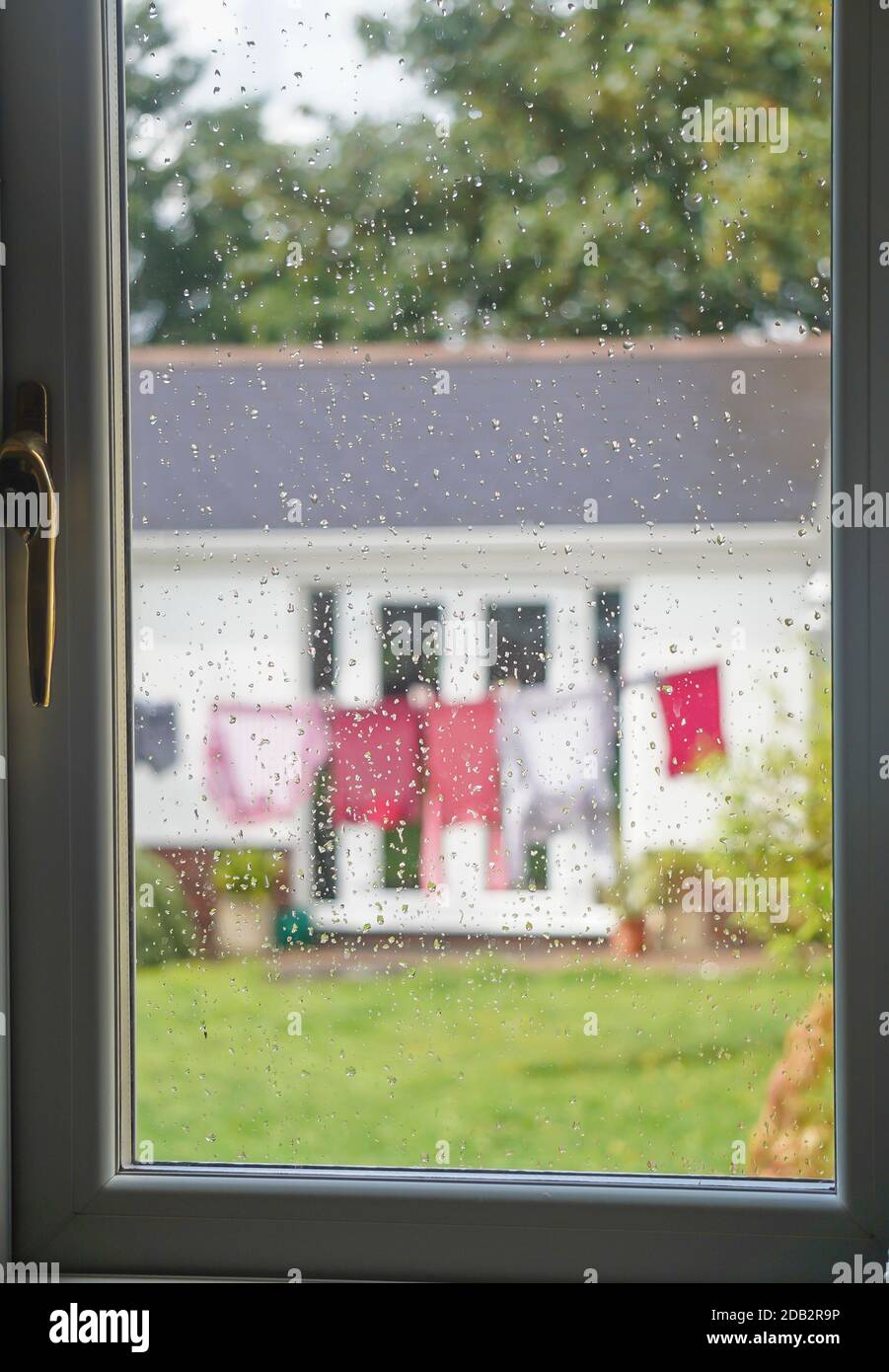 Blick durch das verregnete Küchenfenster eines britischen Hintergartens mit Waschanlagen an einem nassen britischen Sommertag.Großbritannien im Regen! Stockfoto