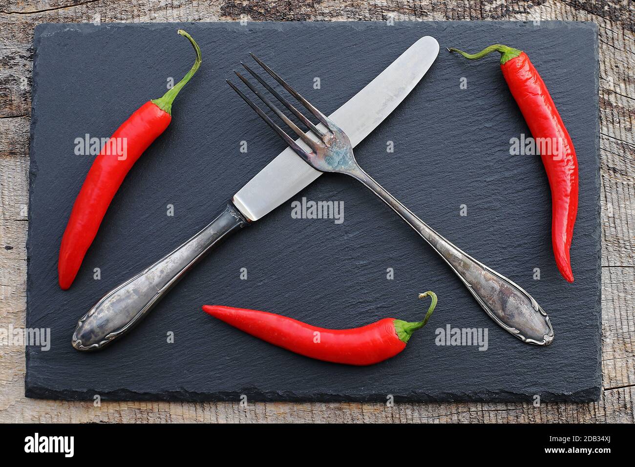 Rote Chilischoten und altes Silberbesteck auf einem schwarzen Schiefertablett Stockfoto