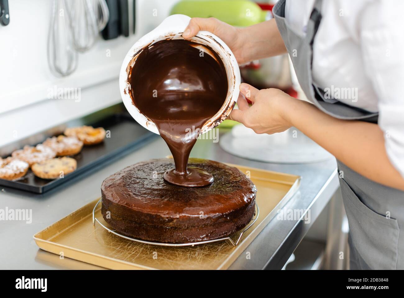 Patissier, die in ihrer Werkstatt flüssige Schokolade auf einen Kuchen gießt Stockfoto