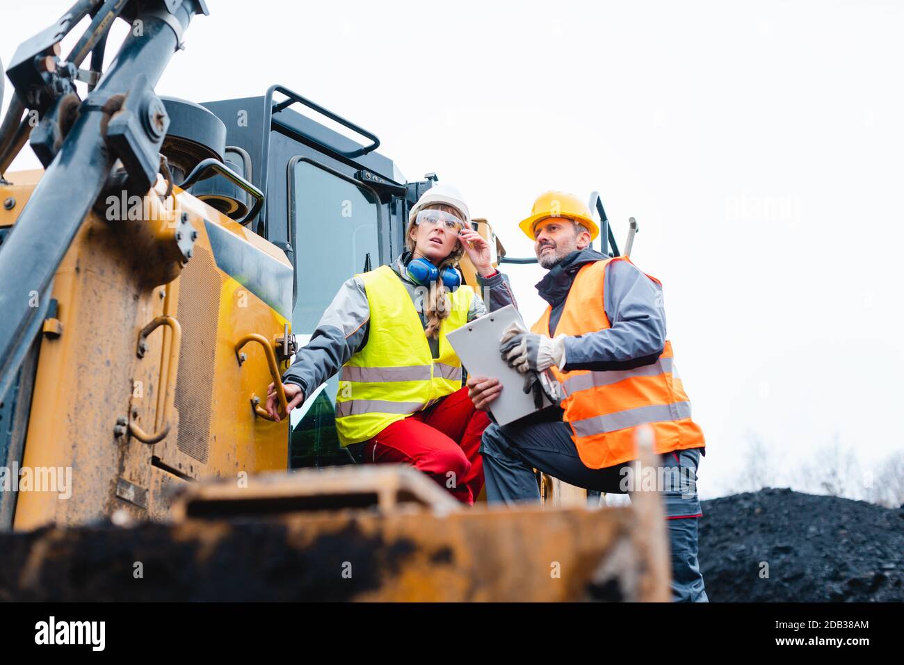 Frau und Mann Arbeiter im Steinbruch auf Aushubmaschine Blick in eine helle Zukunft über dem Horizont Stockfoto