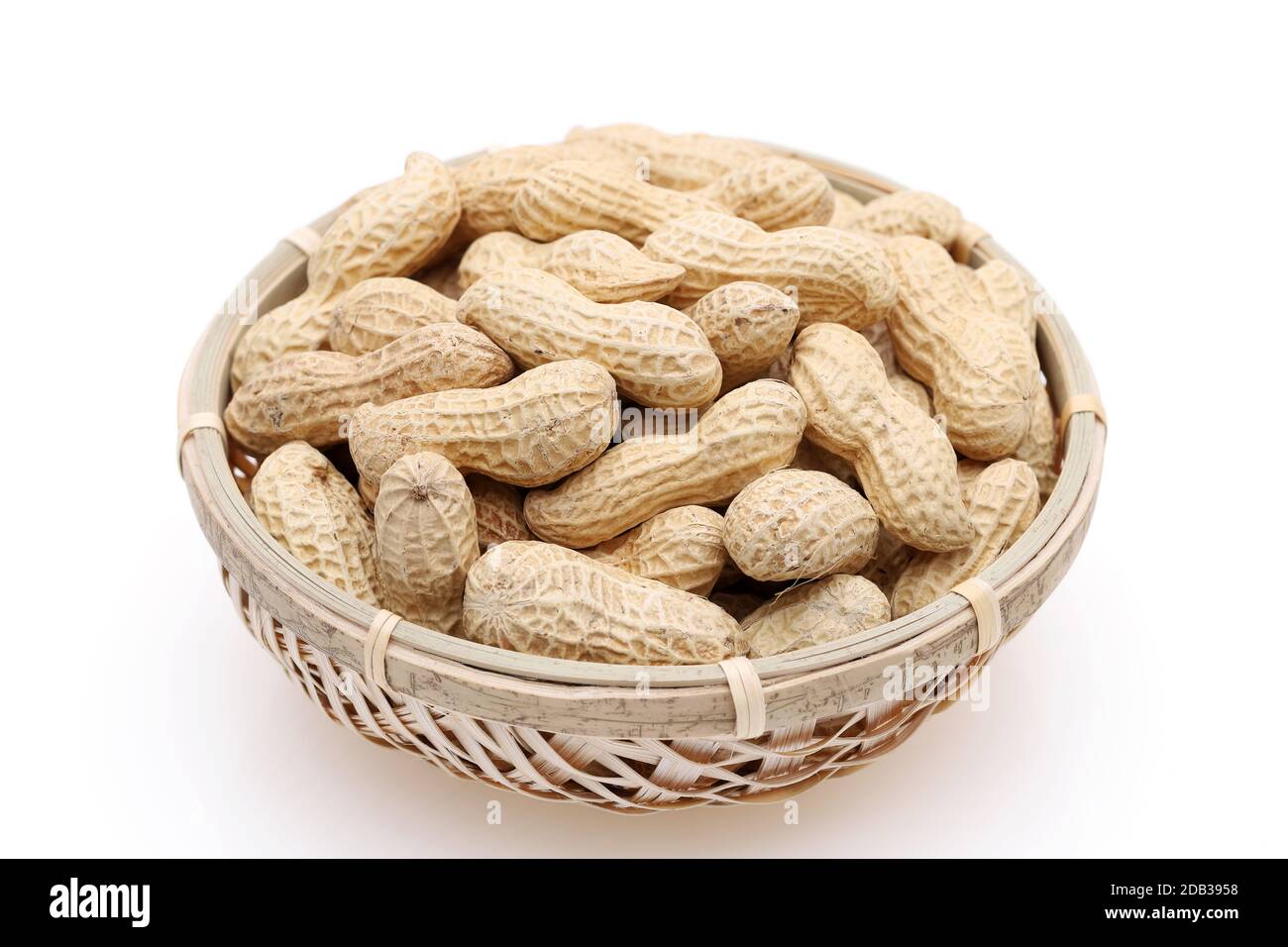 Organische Erdnüsse in der Schale in einem Bambuskorb auf weißem Hintergrund Stockfoto
