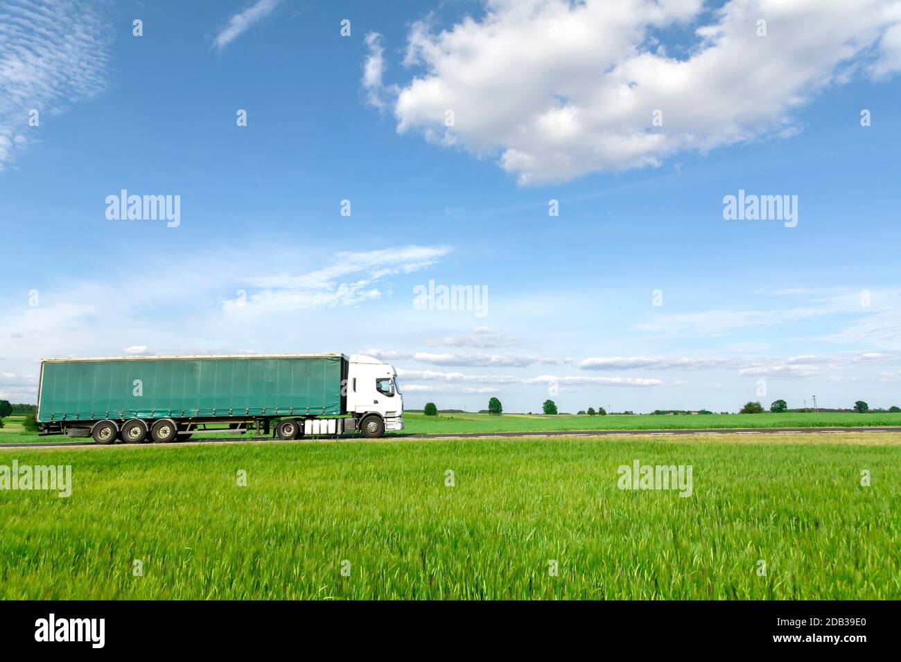 Weißer Transport-LKW fährt auf der Straße, grüne Wiese mit blauem Himmel Stockfoto