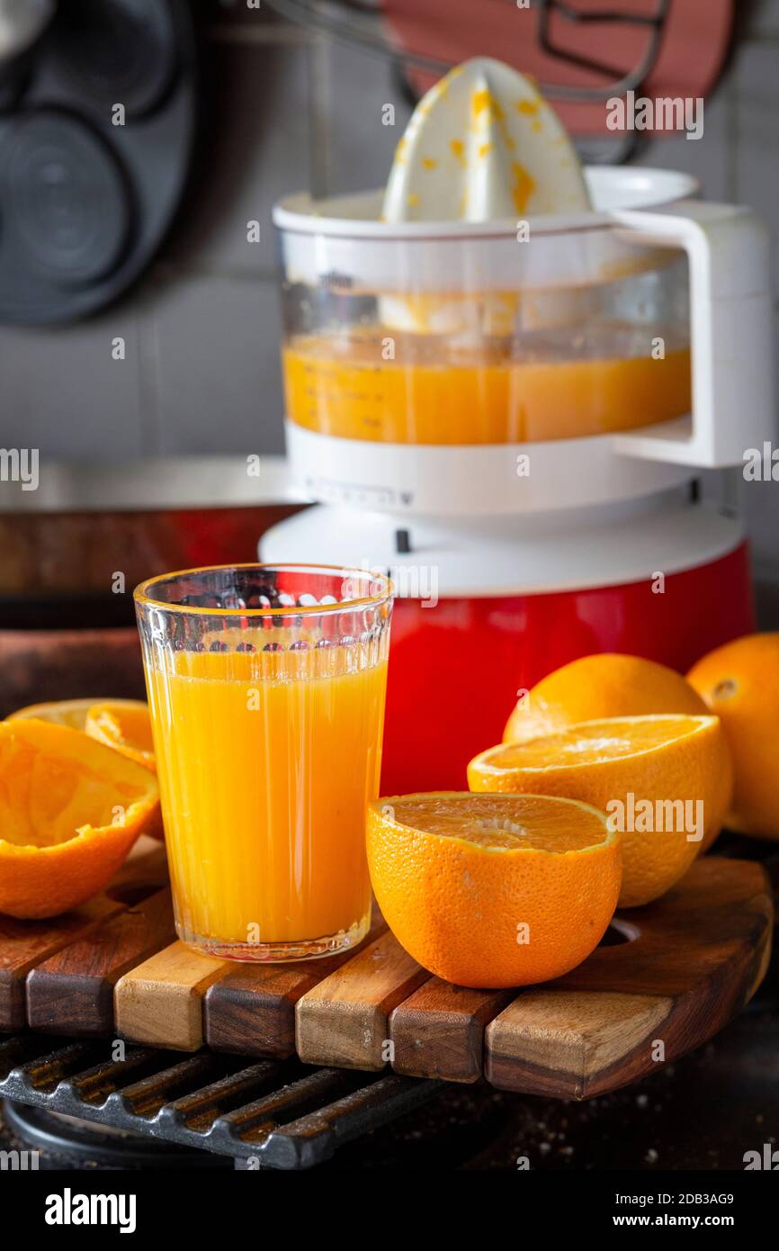 Altmodischer rot-weißer Kunststoffentsafter mit halbierten Orangen zum Entsaften und einem Glas frisch gepresstem Orangensaft - FOODPIX Stockfoto