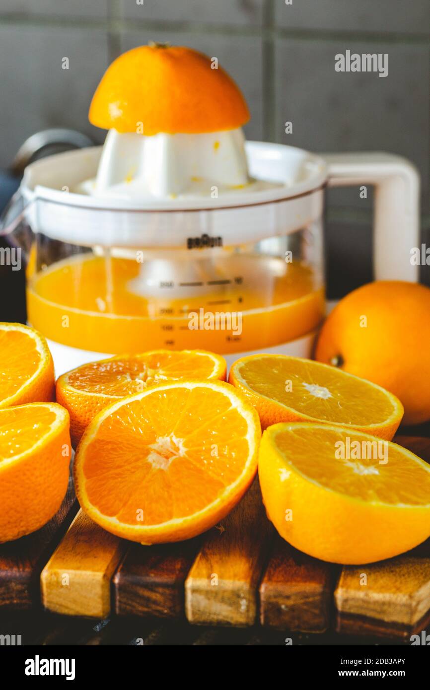Altmodischer rot-weißer Kunststoffentsafter mit halbierten Orangen zum Entsaften und einem Glas frisch gepresstem Orangensaft - FOODPIX Stockfoto