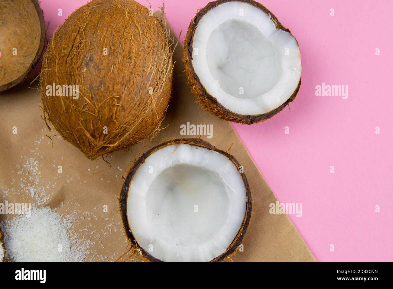 Gebrochene Kokosnüsse auf Bastelpapier, das auf einem rosa Hintergrund steht. Stockfoto