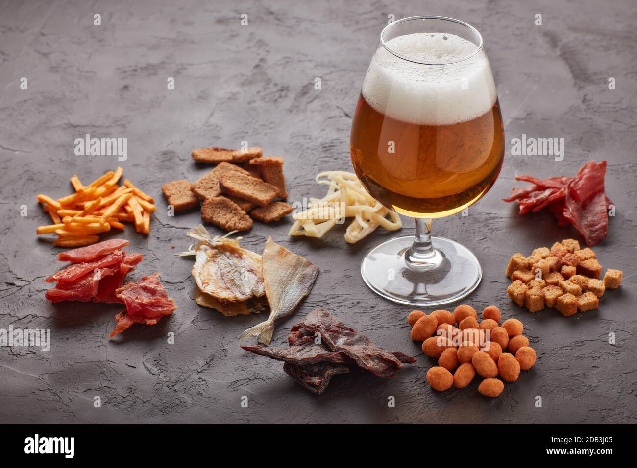 Glas mit Bier und Set von verschiedenen Arten Snacks: Jerky, Kartoffelchips, gesalzene Nüsse, Stockfisch, Brot würzige Cracker, getrocknete Tintenfische auf dunkelgrauem Backgro Stockfoto