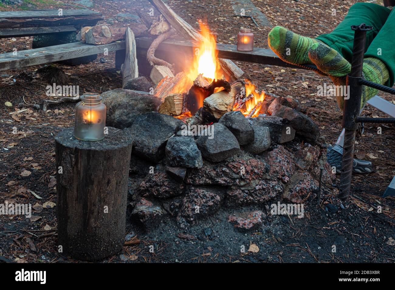Mann im Wald am Feuer wärmt seine Füße in Wollsocken, beschnittenes Foto, Camping-Konzept, Grill. Hochwertige Fotos Stockfoto