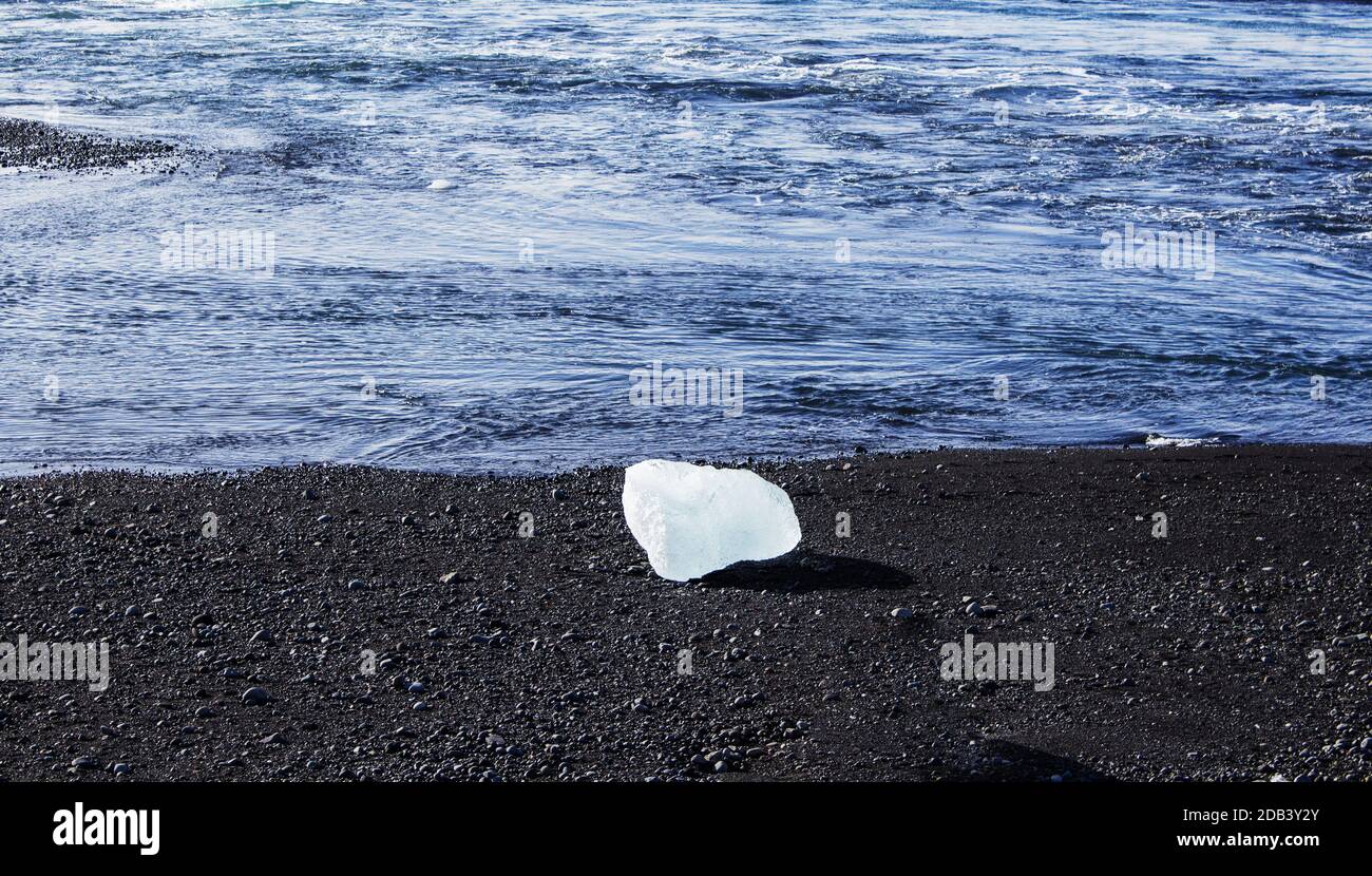 Schwarzer Kieselstrand mit einem einzigen Eisblock vor dem Meer Stockfoto