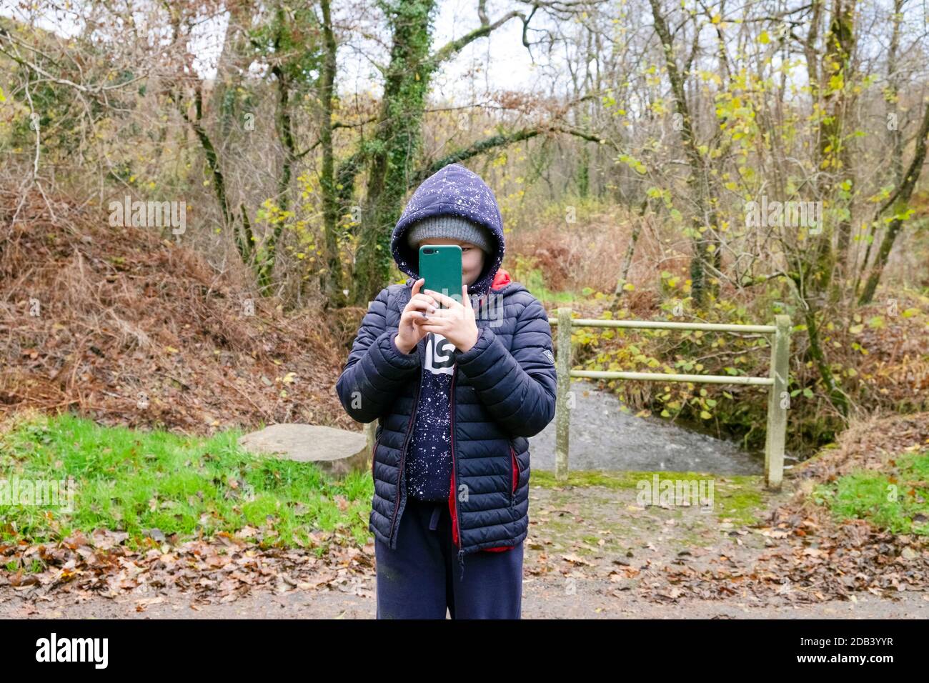 Kind Junge 10 oder 11 Aufnahme Foto mit einem Handy Telefon (Mobiltelefon) Während auf einem Spaziergang im Herbst trägt ein Hoodie und Winterjacke Wales UK KATHY DEWITT Stockfoto