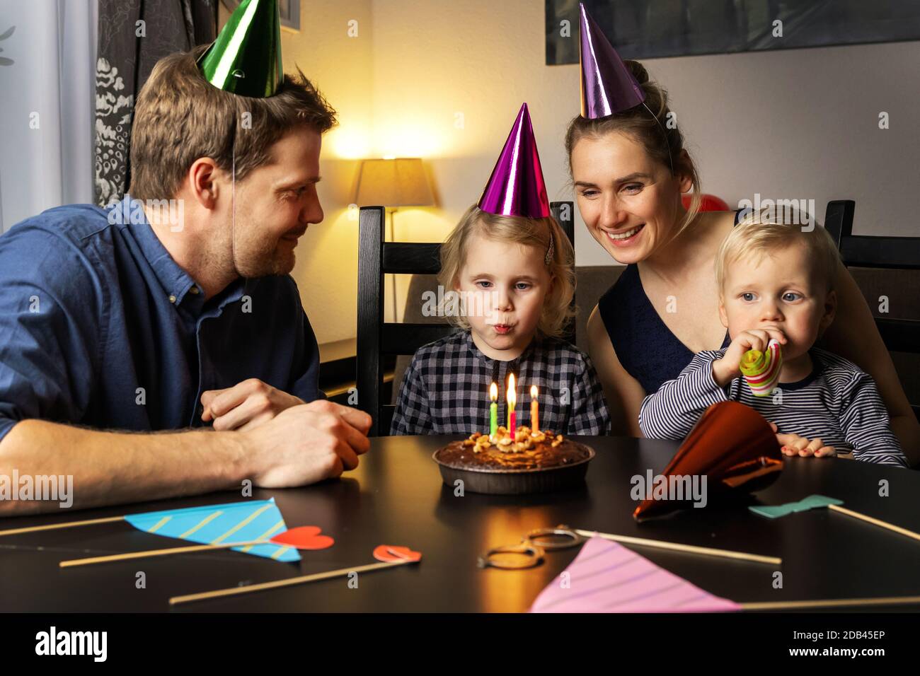 Junge glückliche Familie feiert Tochter Geburtstag zu Hause. Mädchen bläst die Kerzen auf ihrem Kuchen Stockfoto