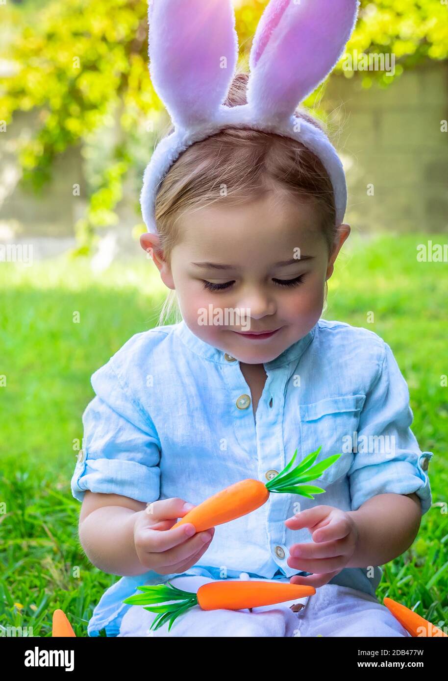 Portrait eines niedlichen kleinen Jungen, der mit Karotten spielt, die als Osterhase verkleidet sind und schöne festliche Furry-Ohren tragen, fröhlicher christlicher Frühlingsurlaub Stockfoto