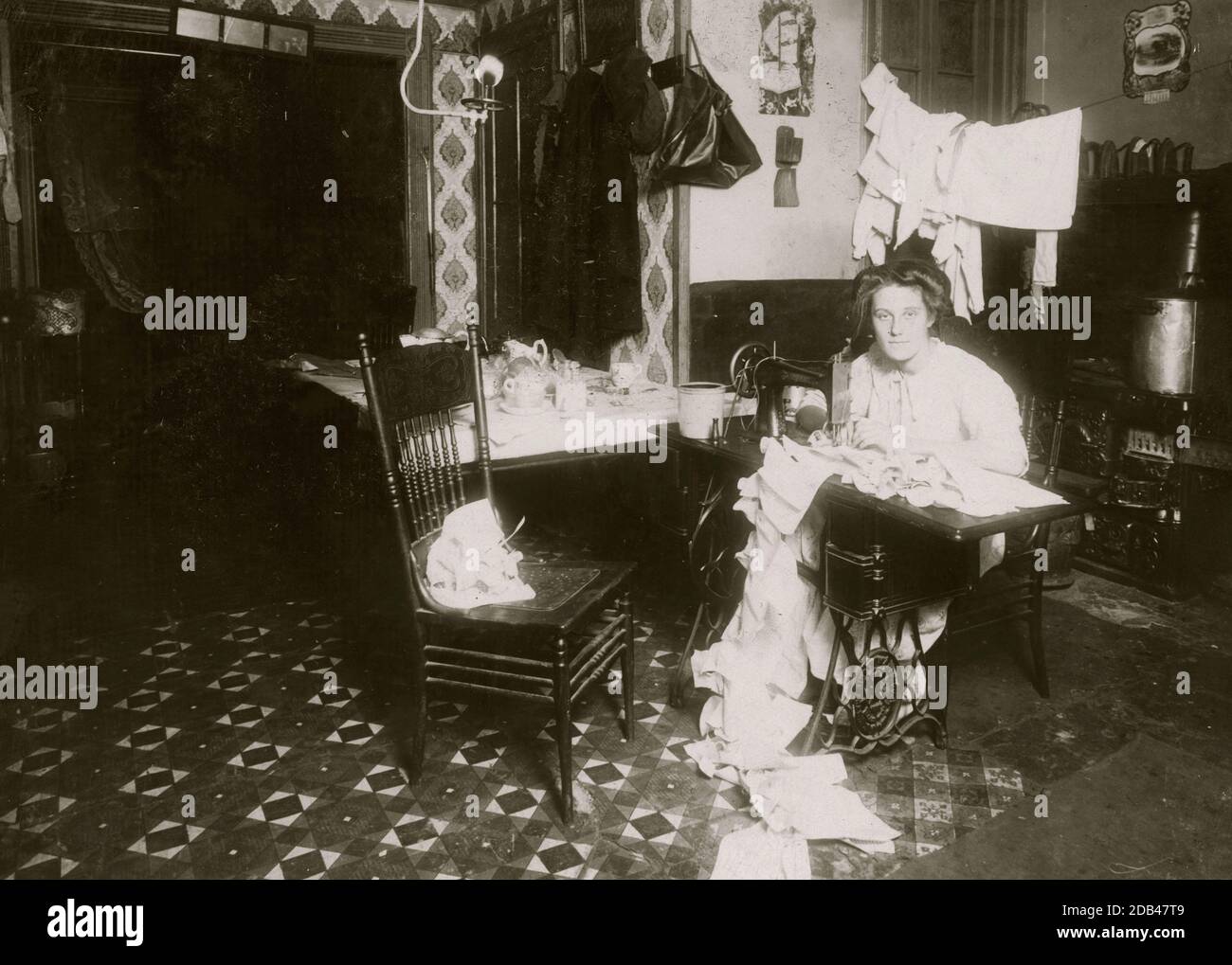 Annie Maier (oder Meyer), die Campbell-Kinderpinafores in ihrem Kellerhaus macht. 71 E. 108 Street. Es wurde berichtet, dass sie an Tuberkulose erkrankt war. Arbeiten in der Küche. Stockfoto