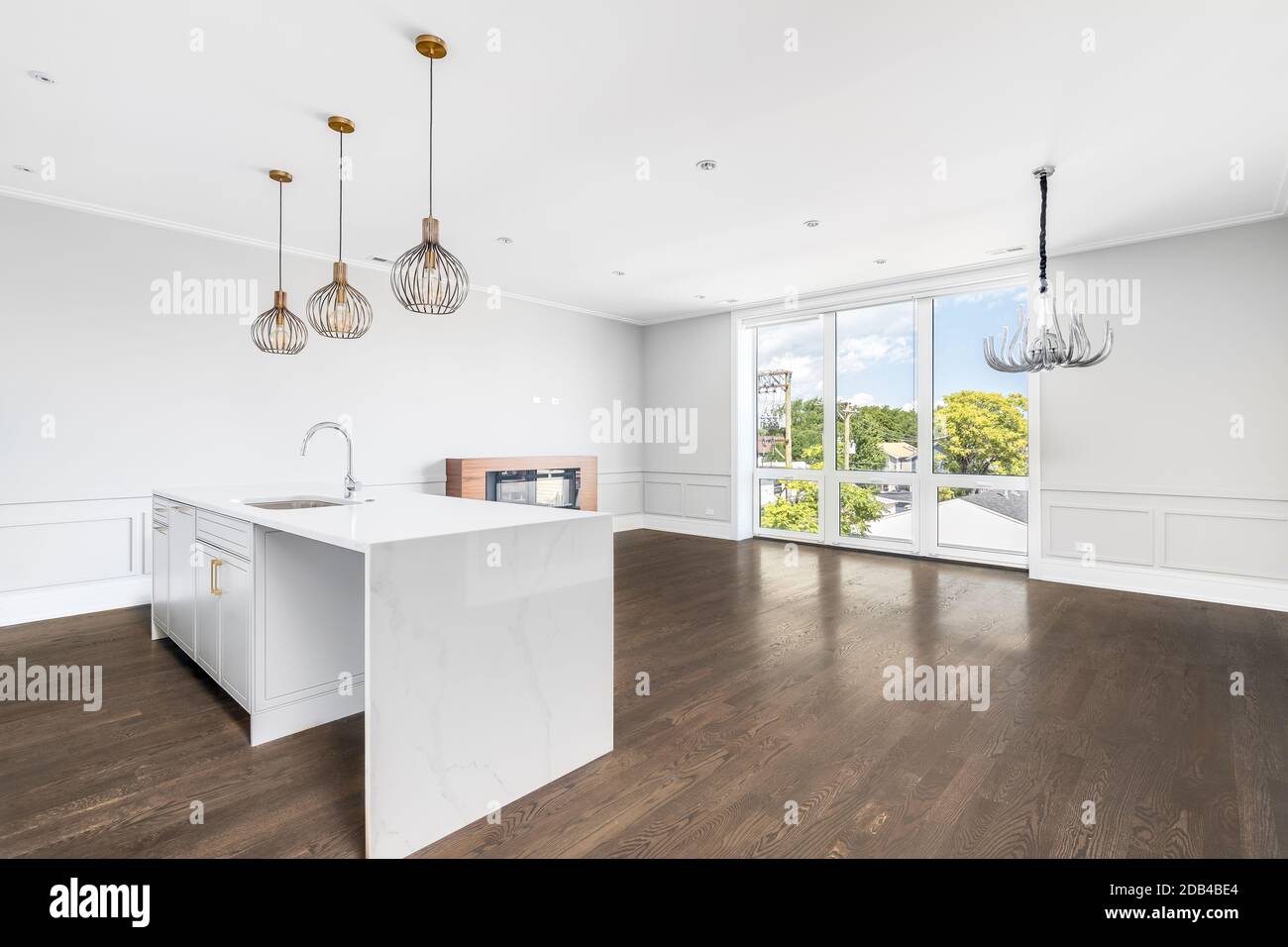 Eine leere, luxuriöse Küche, Esszimmer und Wohnzimmer mit goldenen Lampen, einem Kamin und Kronleuchter über den Hartholzböden. Stockfoto