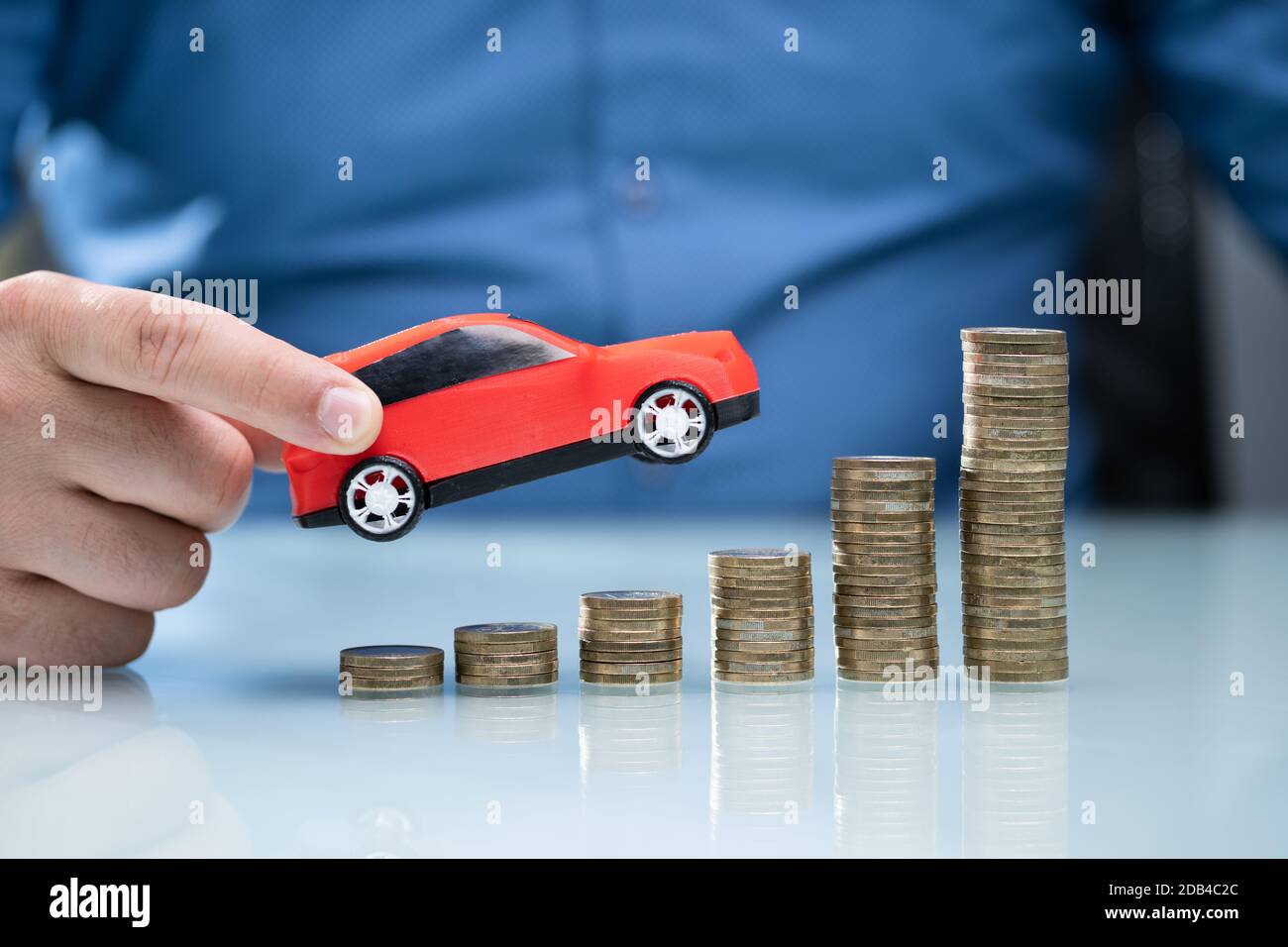 Person, Die Red Car Über Steigende Gestapelte Münzen Hält Stockfoto