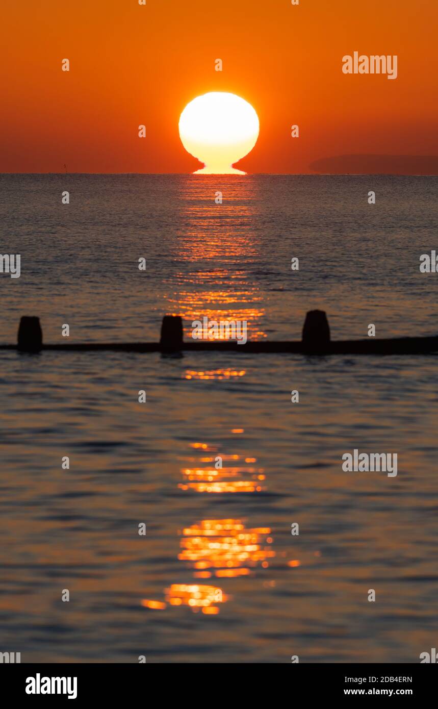 Porträt eines tiefen Sonnenuntergangs über dem Meer. Vertikal des Sonnenuntergangs über dem Meer mit Sonne, die das Wasser berührt. Stockfoto