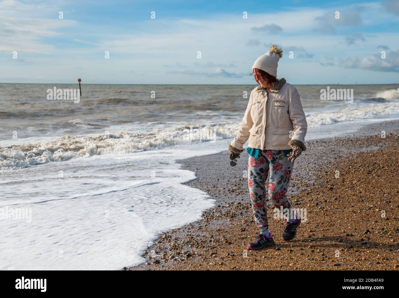 Ältere Frau in Mantel, Hut, Handschuhe und Hose, zu Fuß auf einem Strand am Meer im Herbst in Großbritannien. Strandpromenade. Stockfoto