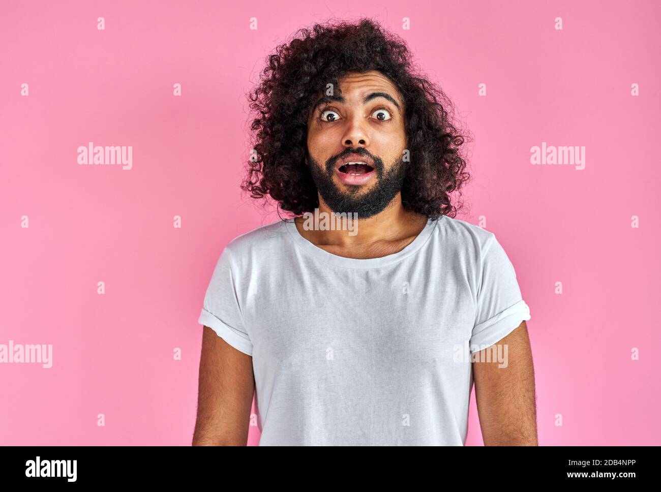 Junge arabische Mann ist schockiert, zeigen Überraschung und erstaunt Ausdruck. Schöner Kerl mit langen lockigen Haaren und Bart bleiben in Schock, isoliert auf rosa Hintergrund Stockfoto