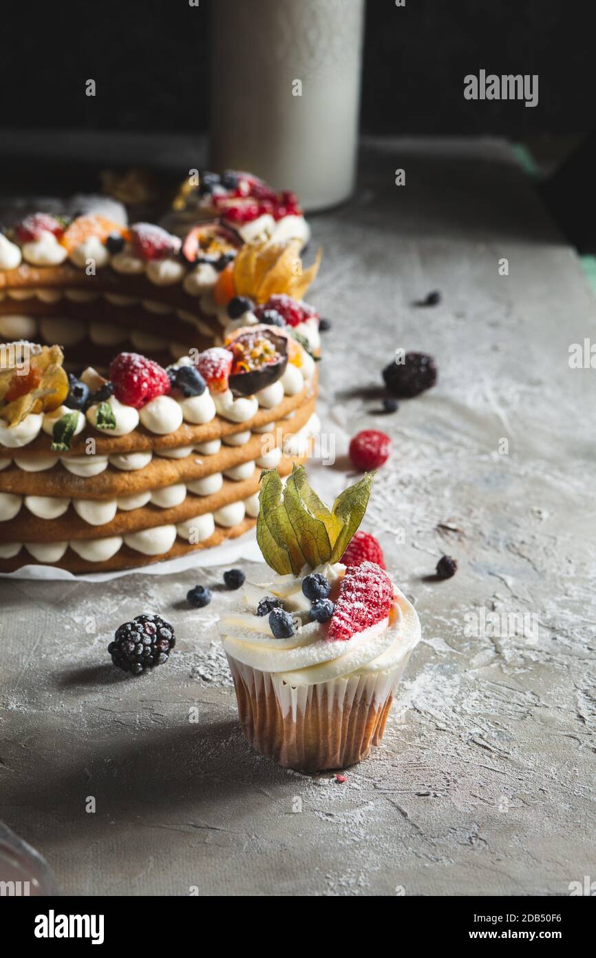 Runde Torte mit Beeren und Cupcake auf grauem Hintergrund Stockfoto