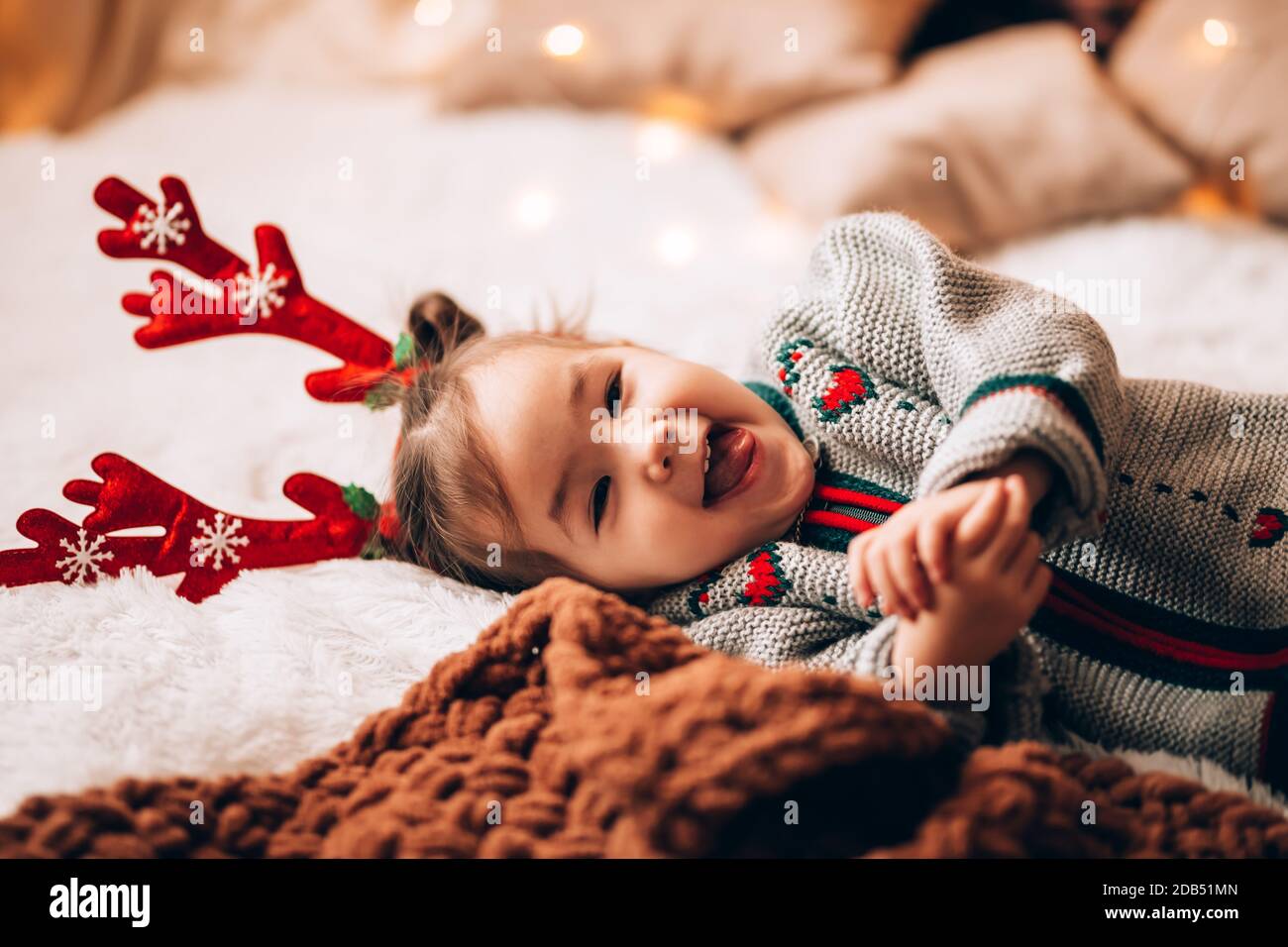 Kleines Mädchen liegt auf einem großen Bett. Das Kind hat Geweihe auf dem Kopf. Weihnachtsstimmung. Stockfoto