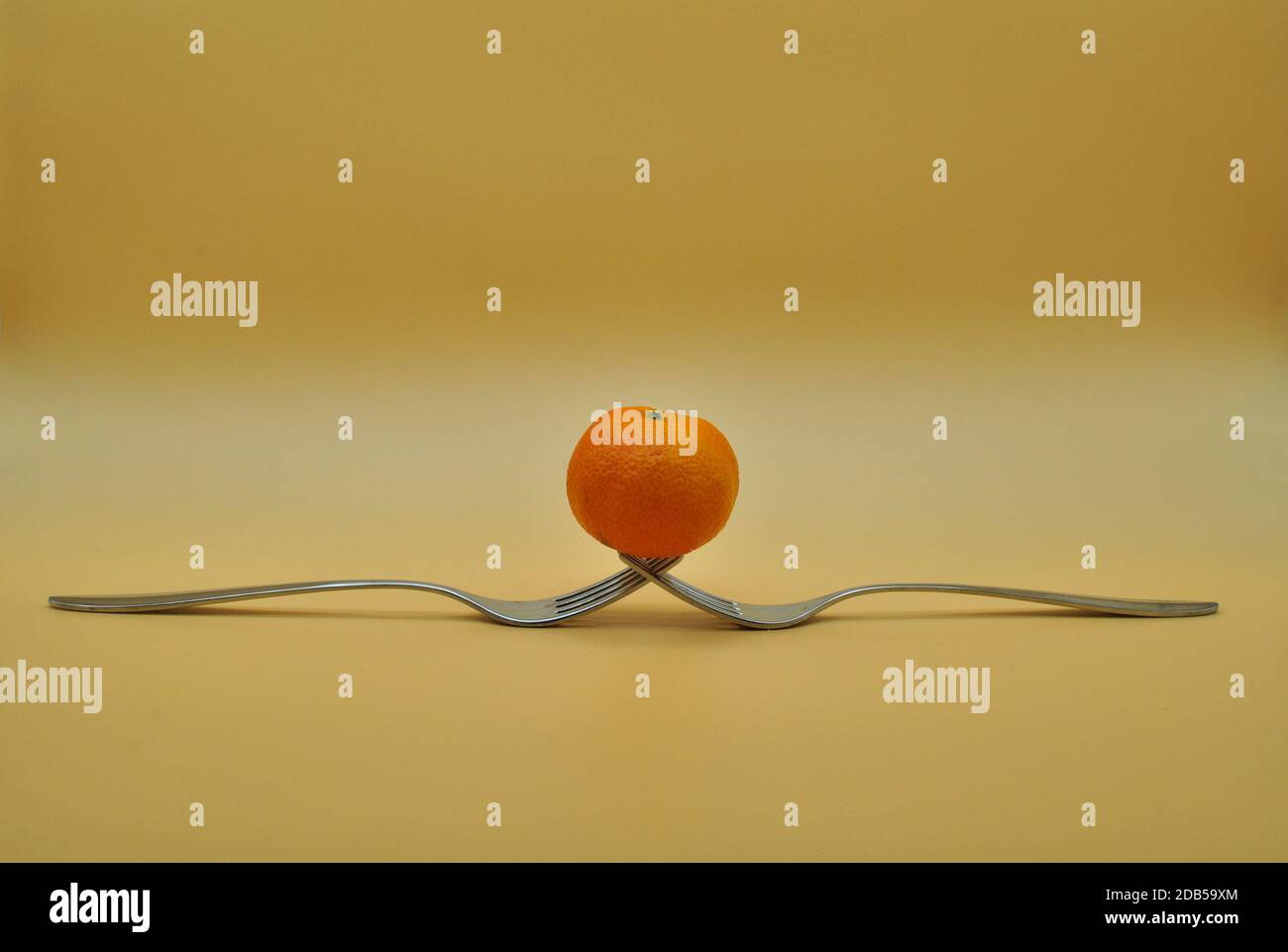 Mandarine ausgeglichen auf einer Zusammensetzung von 2 verflochtenen Gabeln isoliert Über neutralem orangefarbenem Hintergrund Stockfoto