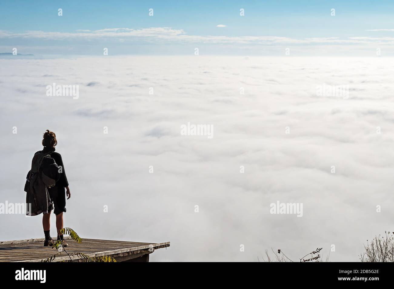 Frau, die auf einer hölzernen Plattform steht und den Blick auf das nebelbedeckte Tal unten genießt. Wandern, Leistung, Erwartung, Optimismus und Selbstreflexion Stockfoto