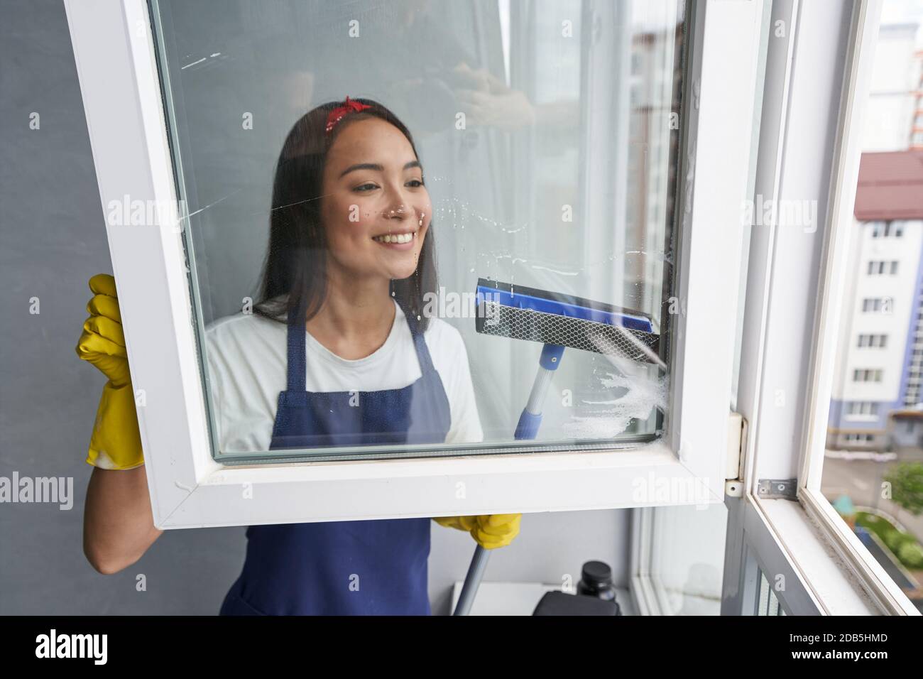 Schnell und effizient. Attraktive junge Frau lächelt beim Reinigen des Fensters mit Rakel. Hausarbeit und Housekeeping, Reinigungsdienstkonzept Stockfoto