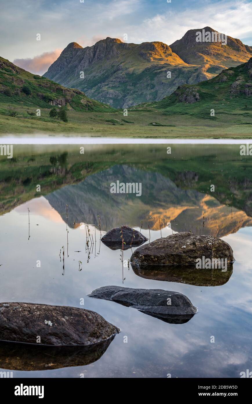 Morgensonne trifft Berggipfel mit Spiegelungen im See. Blea Tarn, Lake District, Großbritannien. Stockfoto