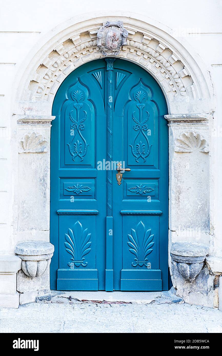 Historisches Eingangsportal mit verwittertem Wappen. Torbogen reich mit Ornamenten mit einer zweiblättrigen blauen Holztür verziert. Stockfoto