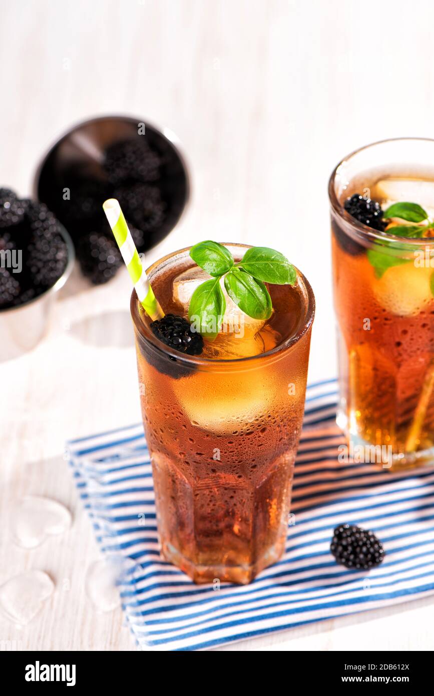 Das Glas Eistee mit Brombeere auf Holztisch. Cuba Libre oder Long Island Cocktail, kaltes Getränk oder Limonade mit Zitrone und Basilikum. Stockfoto