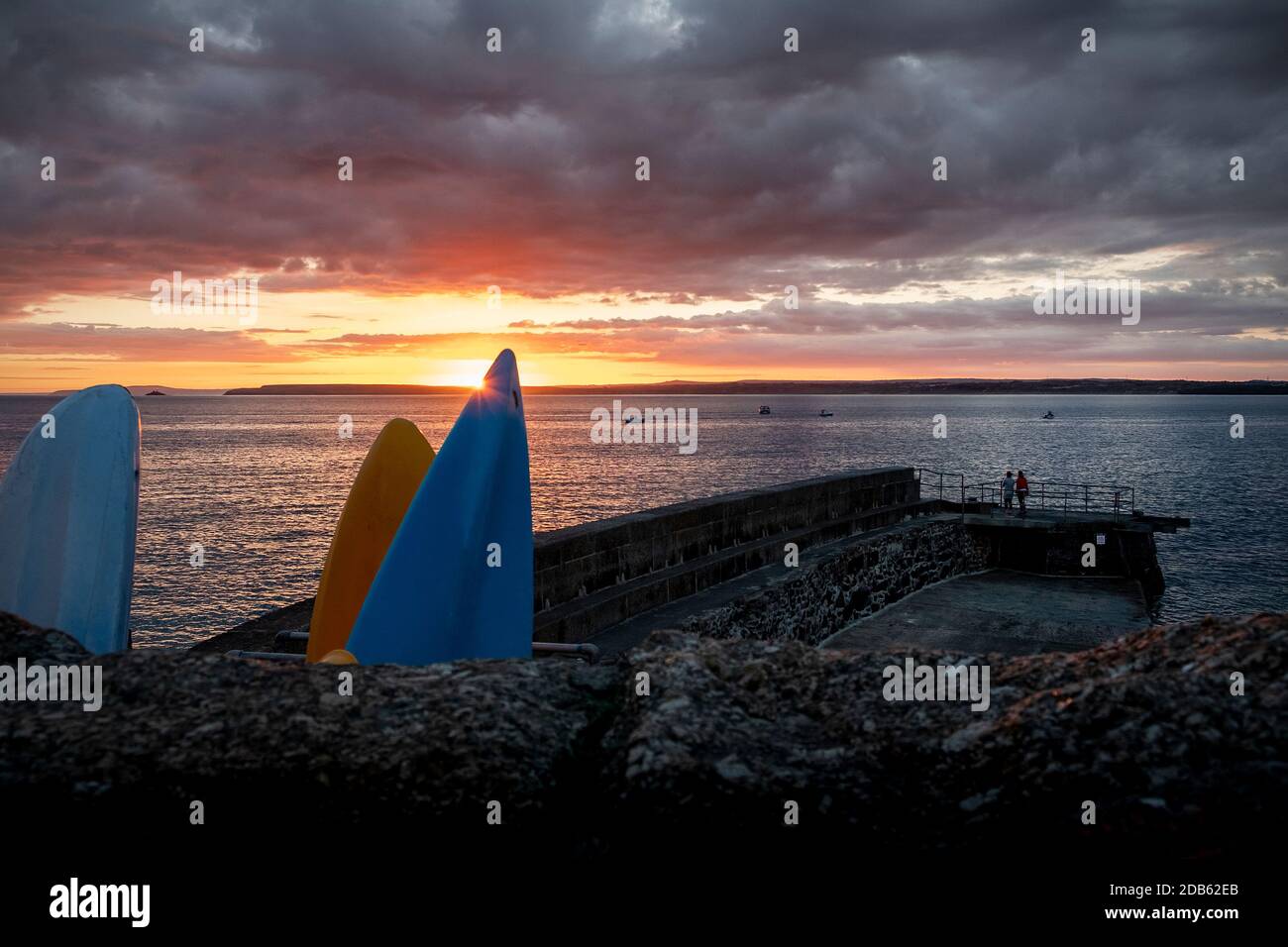 2 Personen beobachten einen Sommeraufgang über Godrevy Point, St Ives Bay mit Godrevy Leuchtturm in der Ferne. St. Ives alter Hafen. Stockfoto
