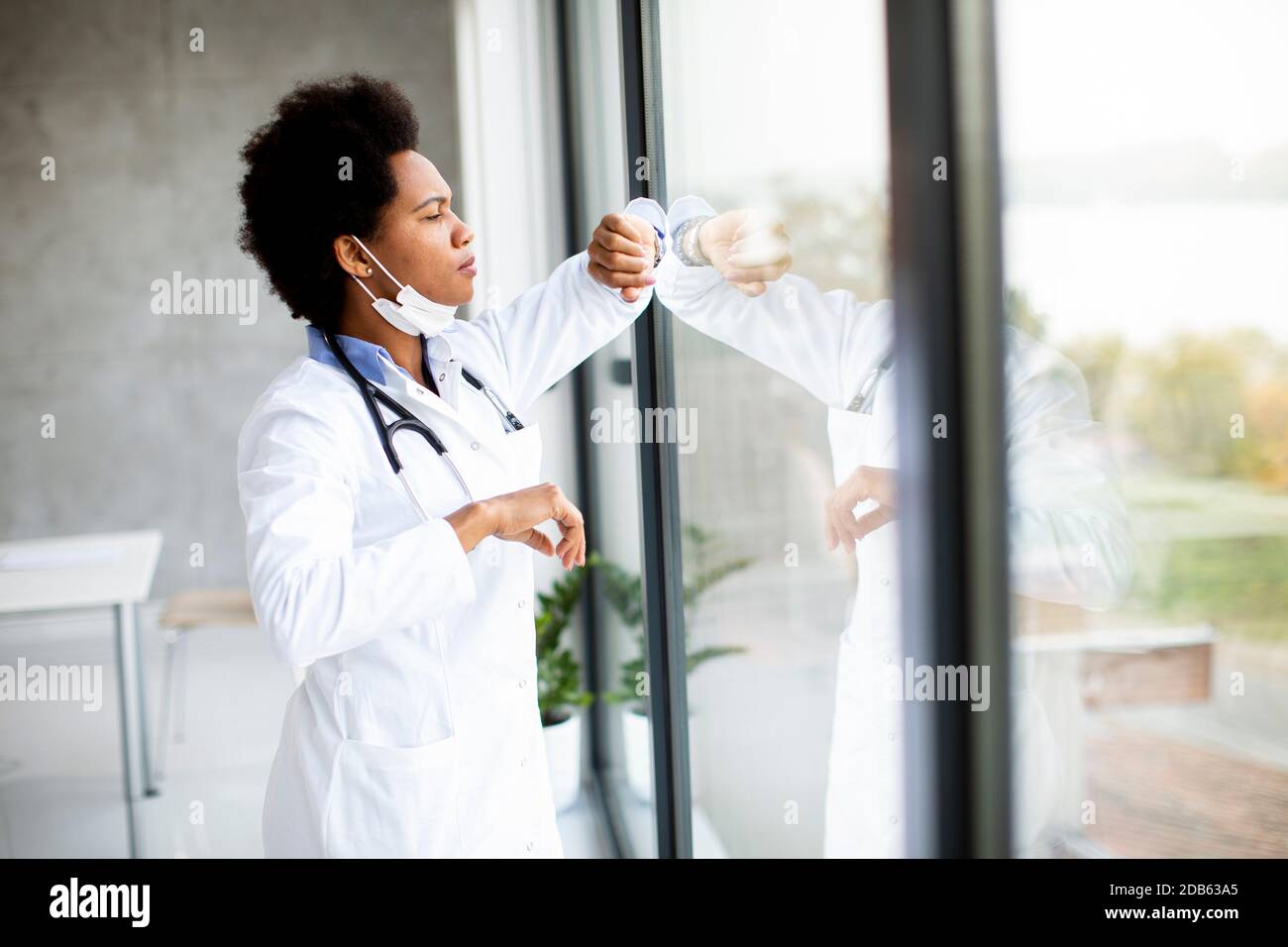 Schwarze Ärztin steht neben dem medizinischen Büro Fenster und Zeitkontrolle auf der Uhr Stockfoto