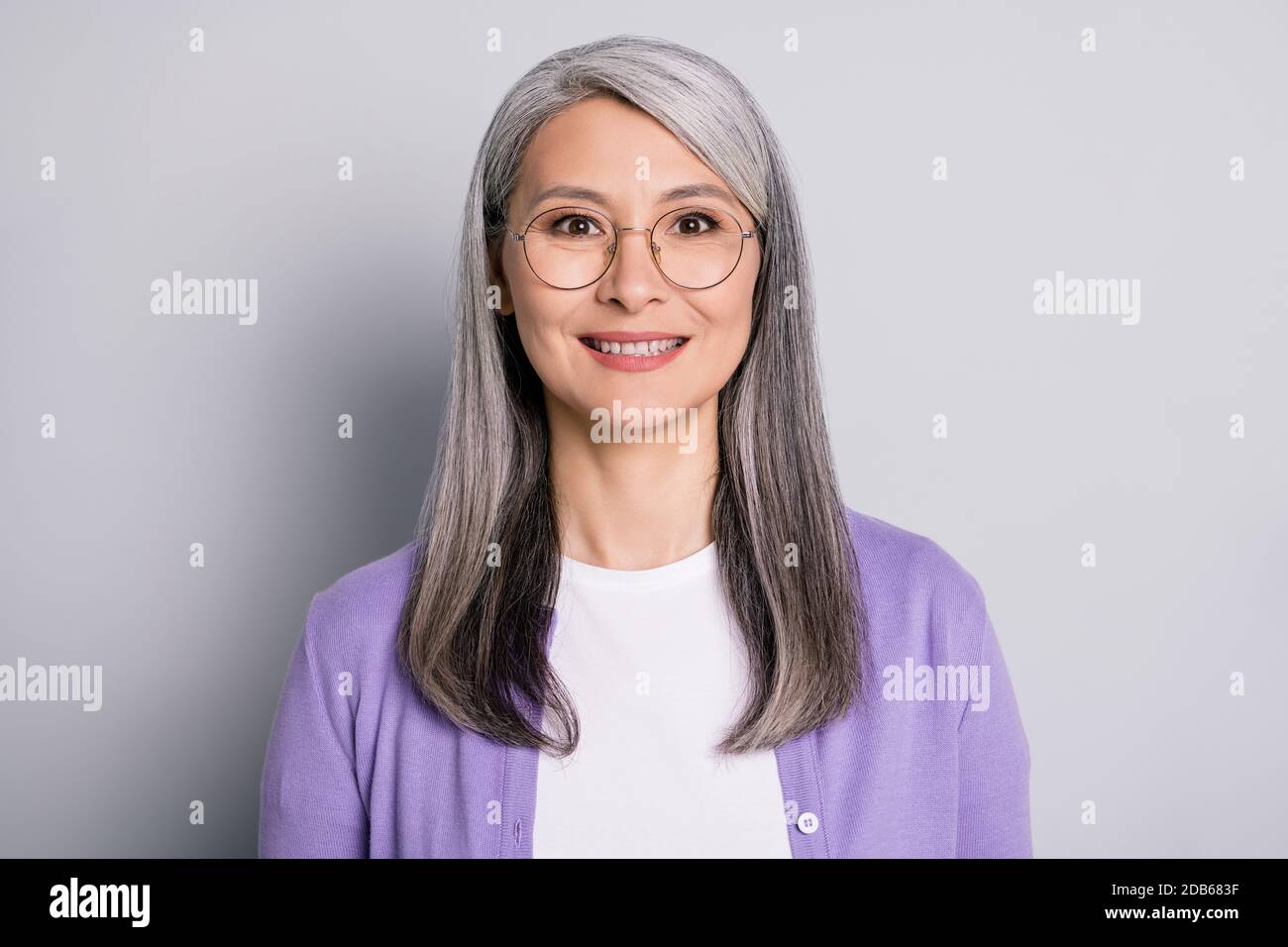 Portraitfoto von positiv lächelnden älteren Frau trägt Brillen und Lila Strickjacke isoliert auf grauem Hintergrund Stockfoto