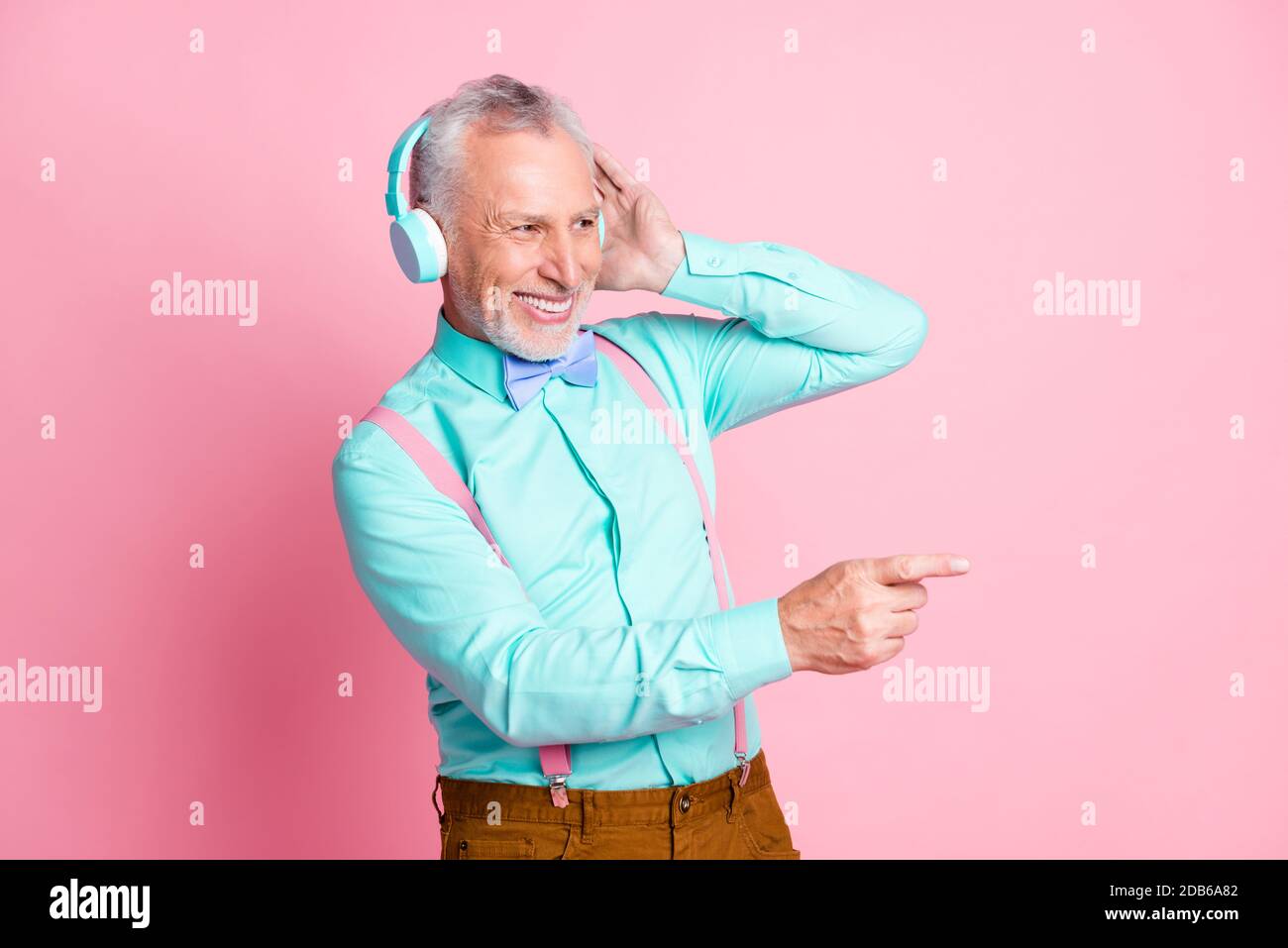 Portrait Foto von alten Gentleman Musik hören mit Wireless Kopfhörer zeigen mit Finger isoliert auf rosa Hintergrund Stockfoto