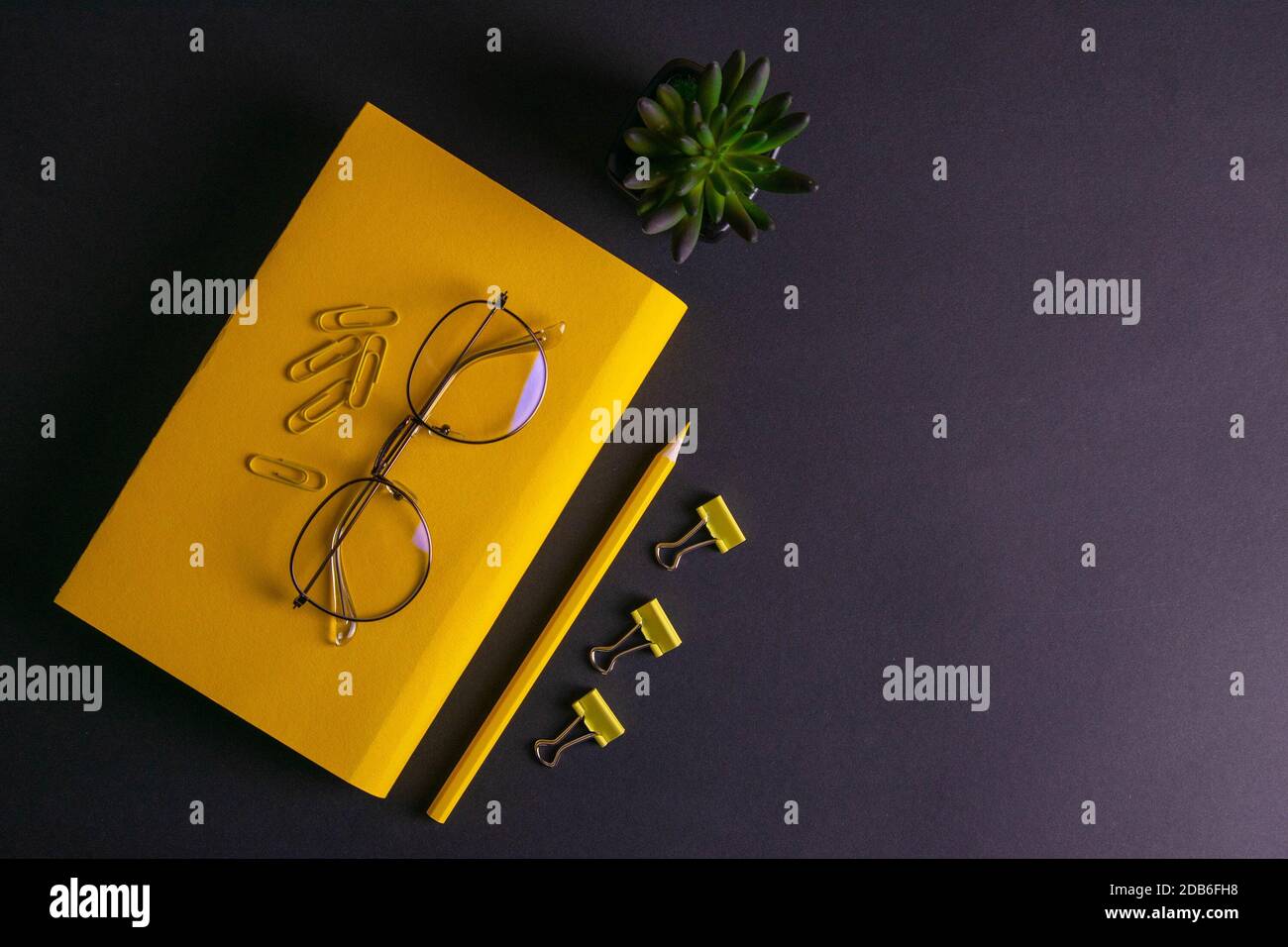 Gelber Bleistift, gelbes Notizbuch und Brille, Stifte, Clip-Papier auf schwarzem Hintergrund. Stockfoto