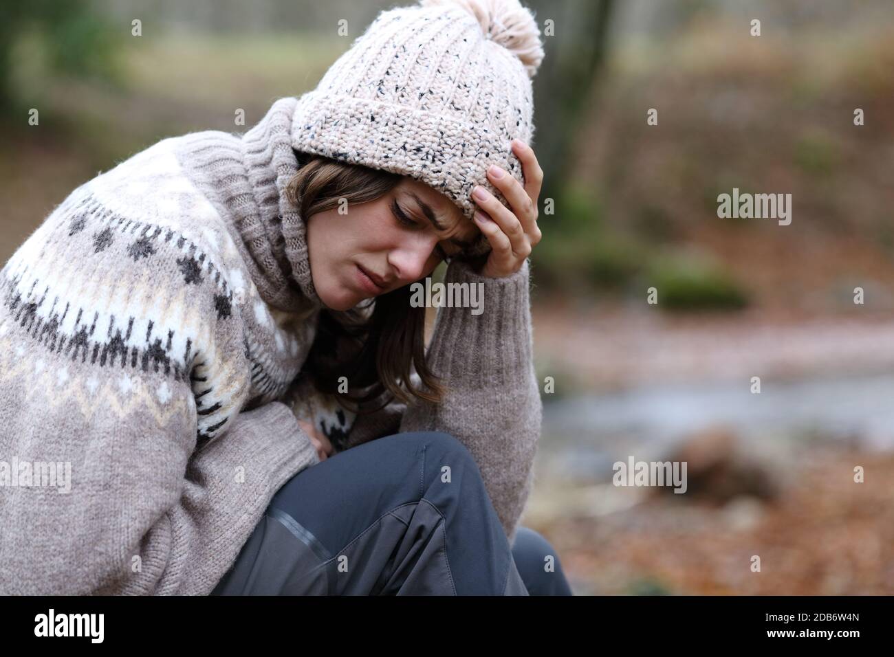 Traurige Frau im Winter beklagt allein sitzen in einem Wald In einem Flussufer Stockfoto