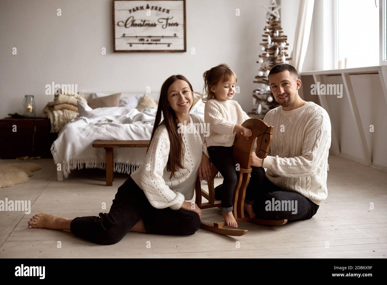 Porträt einer glücklichen Familie. Mama, Papa, ihre Tochter, die auf einem hölzernen Schaukelpferd sitzt, haben Spaß, Weihnachten zu Hause zu feiern. Familie sitzt auf Th Stockfoto