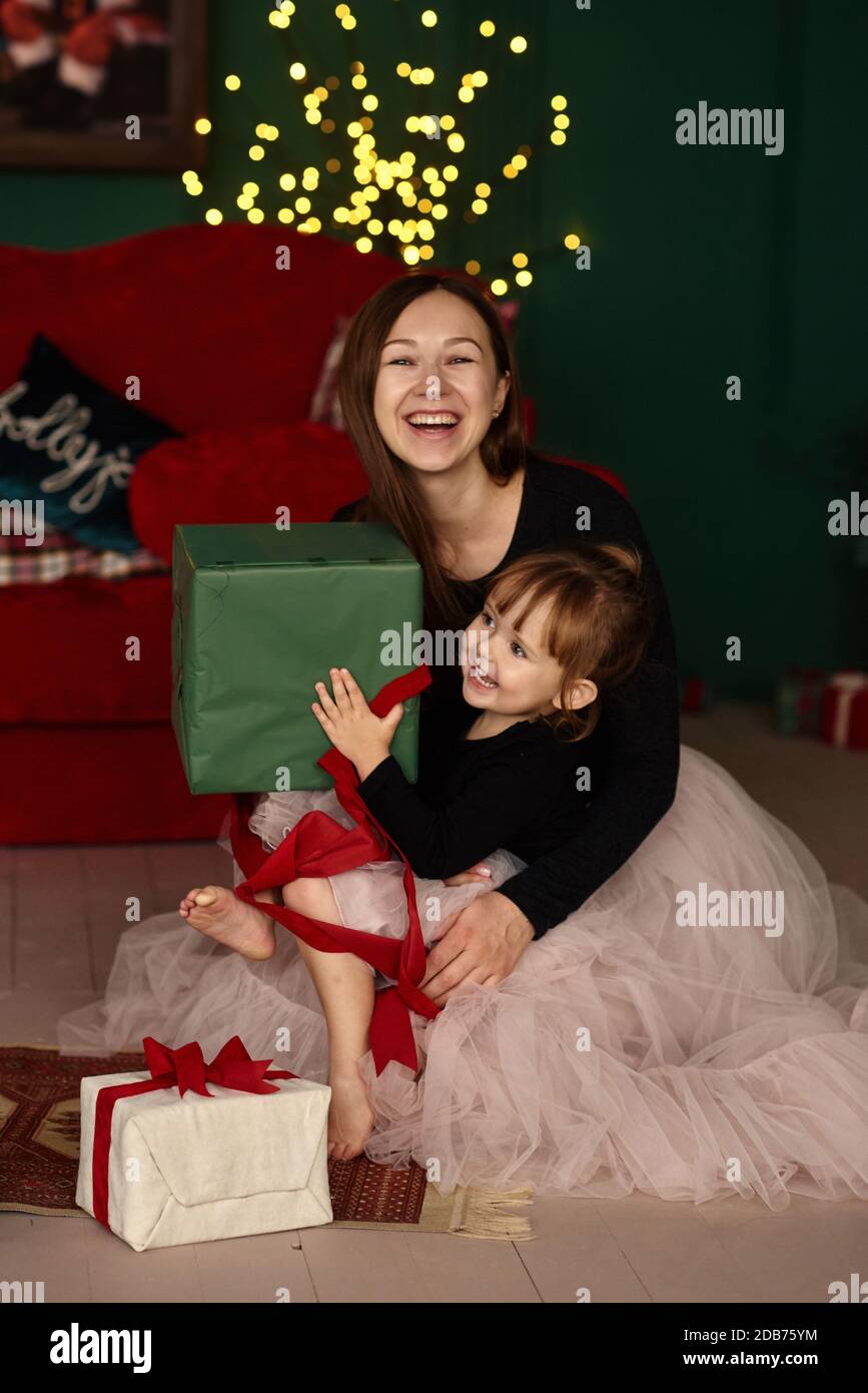 Weihnachtsmorgen. Porträt einer jungen Mutter mit ihrer kleinen Tochter Spaß und Eröffnung Weihnachtsgeschenke sitzen auf dem Boden in einem Raum mit s Stockfoto