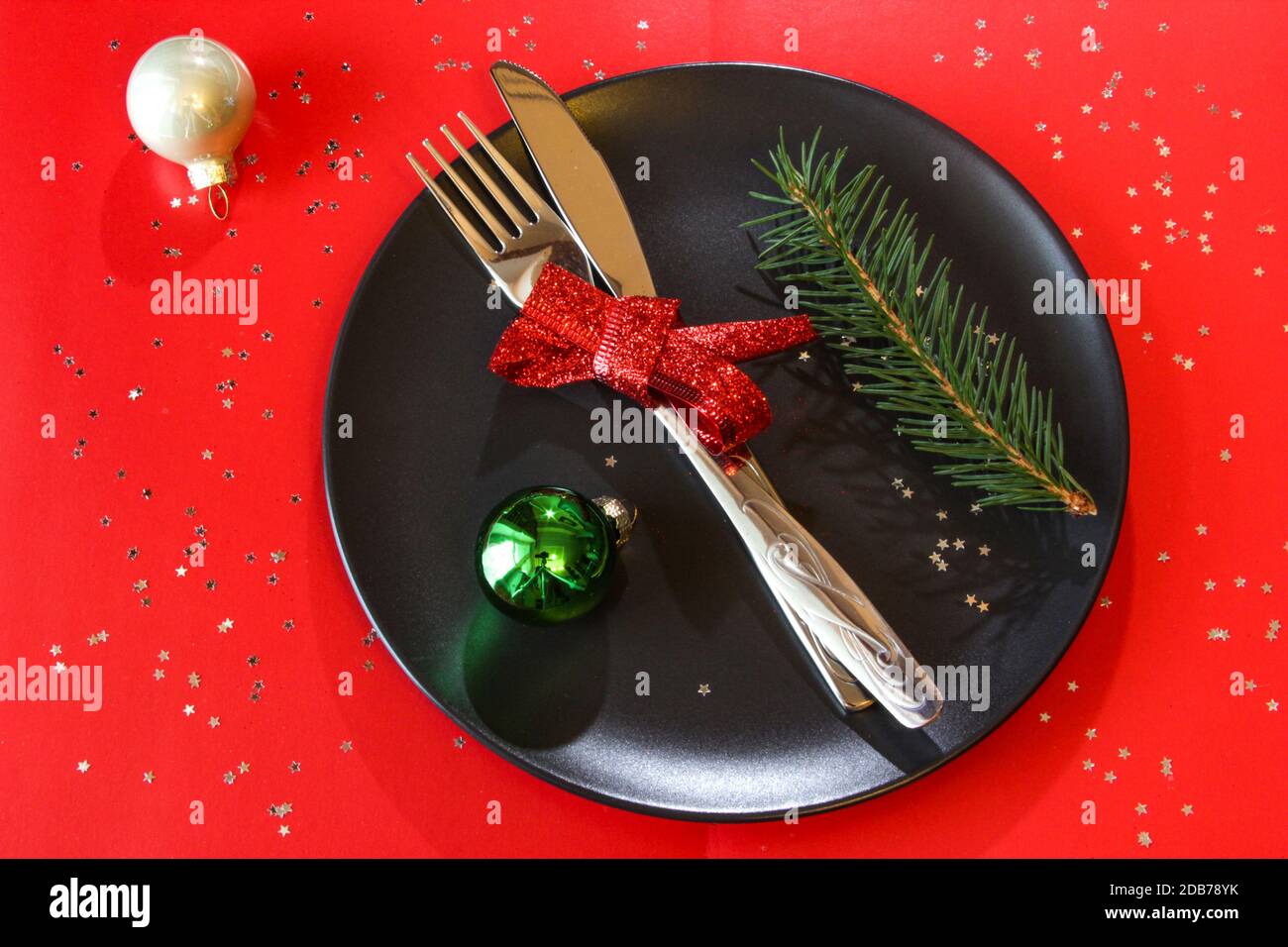 Weihnachtliche Tischeinstellung in schwarzer Platte mit farbigen Kugeln und Sternen auf rotem Tisch, Kopierraum. Weihnachtsessen, Party-Design, Konzept. Stockfoto