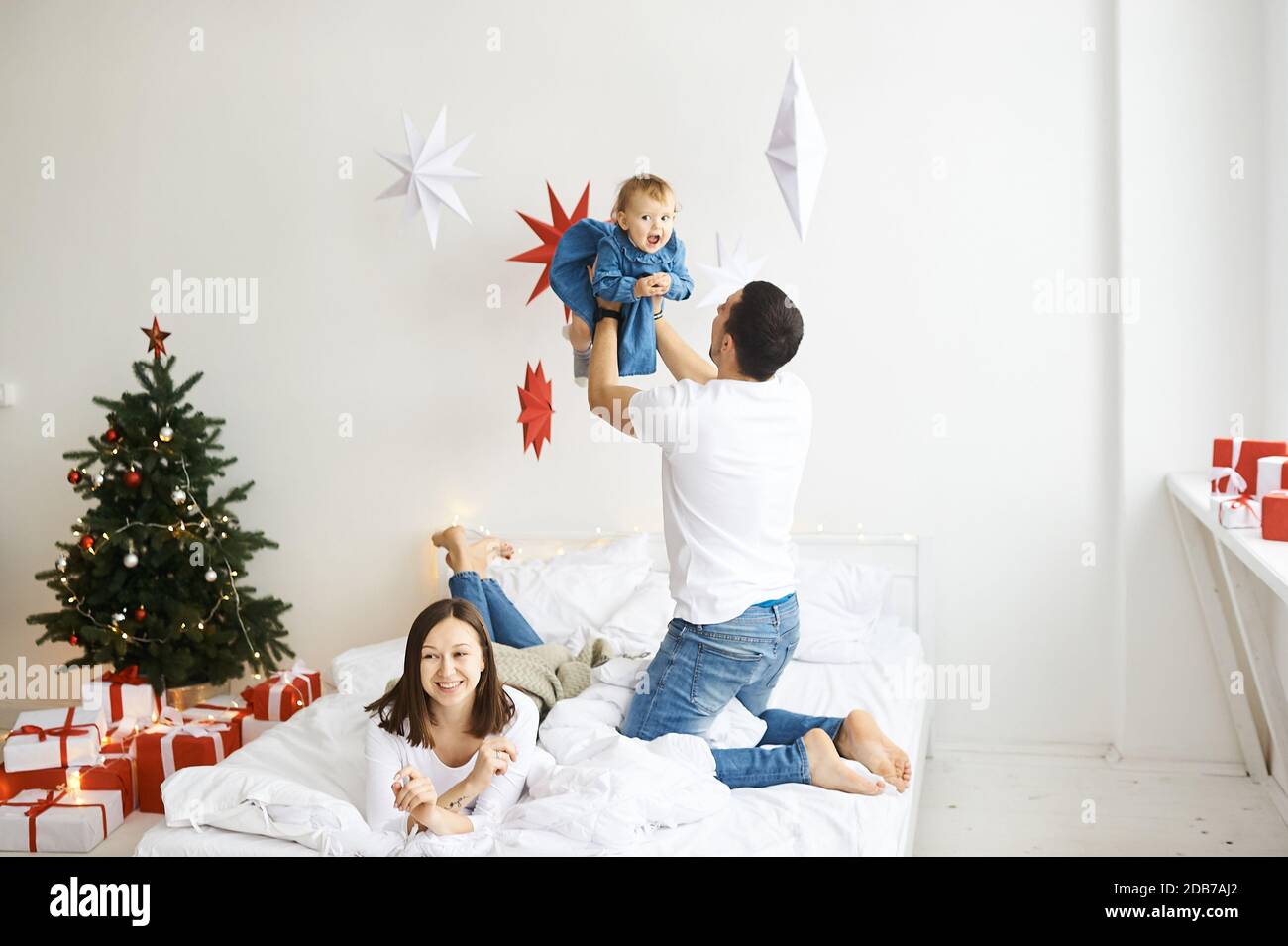 Glückliche Mutter Vater und Tochter spielen auf dem Bett im Schlafzimmer am Weihnachtsmorgen. Stockfoto