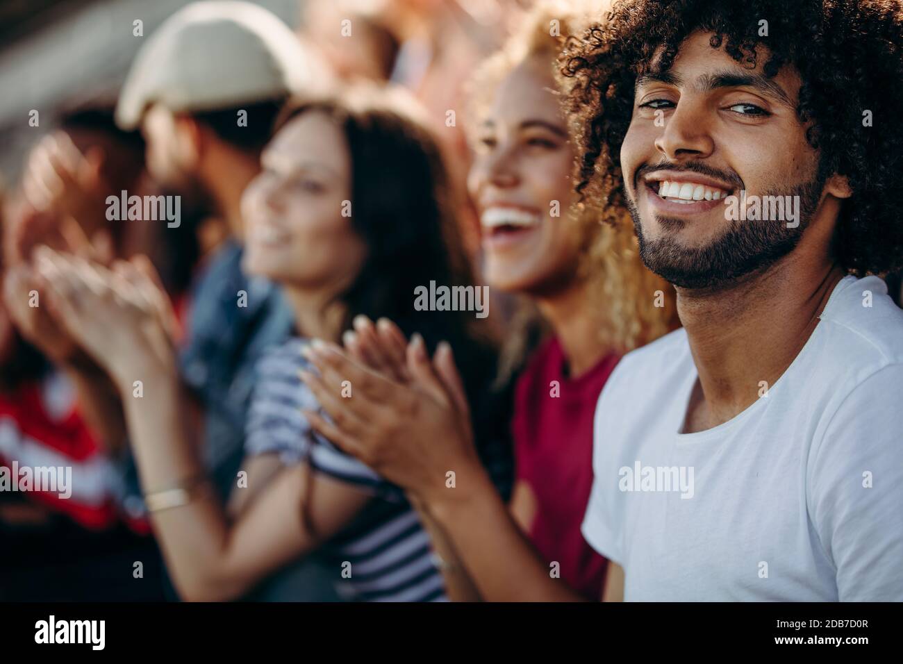 Mann, der mit Freunden sitzt und ein Fußballspiel anschaut und im Stadion applaudiert. Gruppe von jungen Leuten, die ein Fußballspiel beobachten. Stockfoto