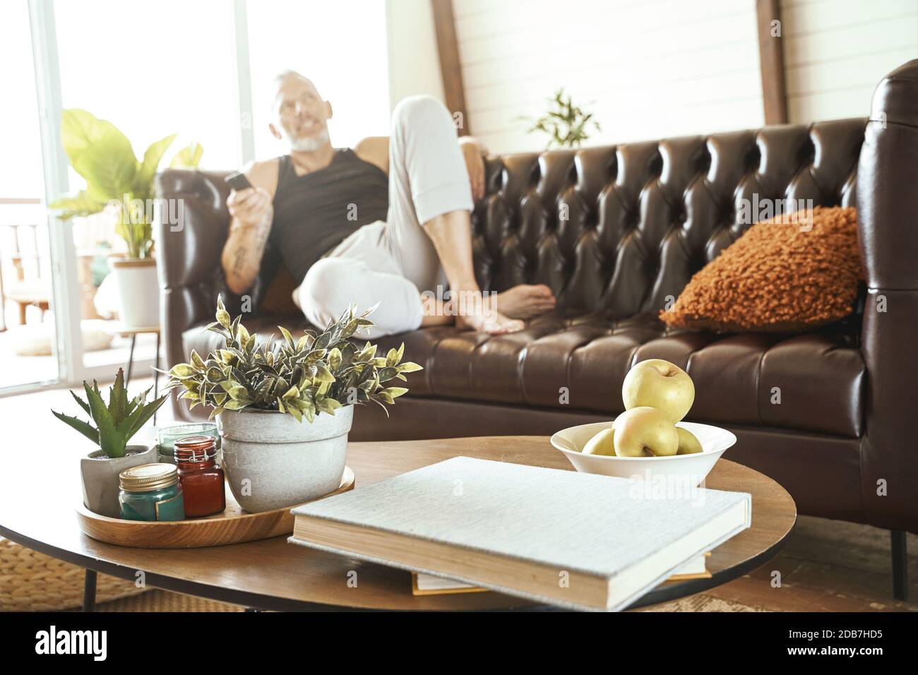 Mann mittleren Alters in legerer Kleidung mit Smartphone in der Hand Entspannen Sie sich auf einem bequemen Sofa im Wohnzimmer, konzentrieren Sie sich auf den kleinen Couchtisch Stockfoto