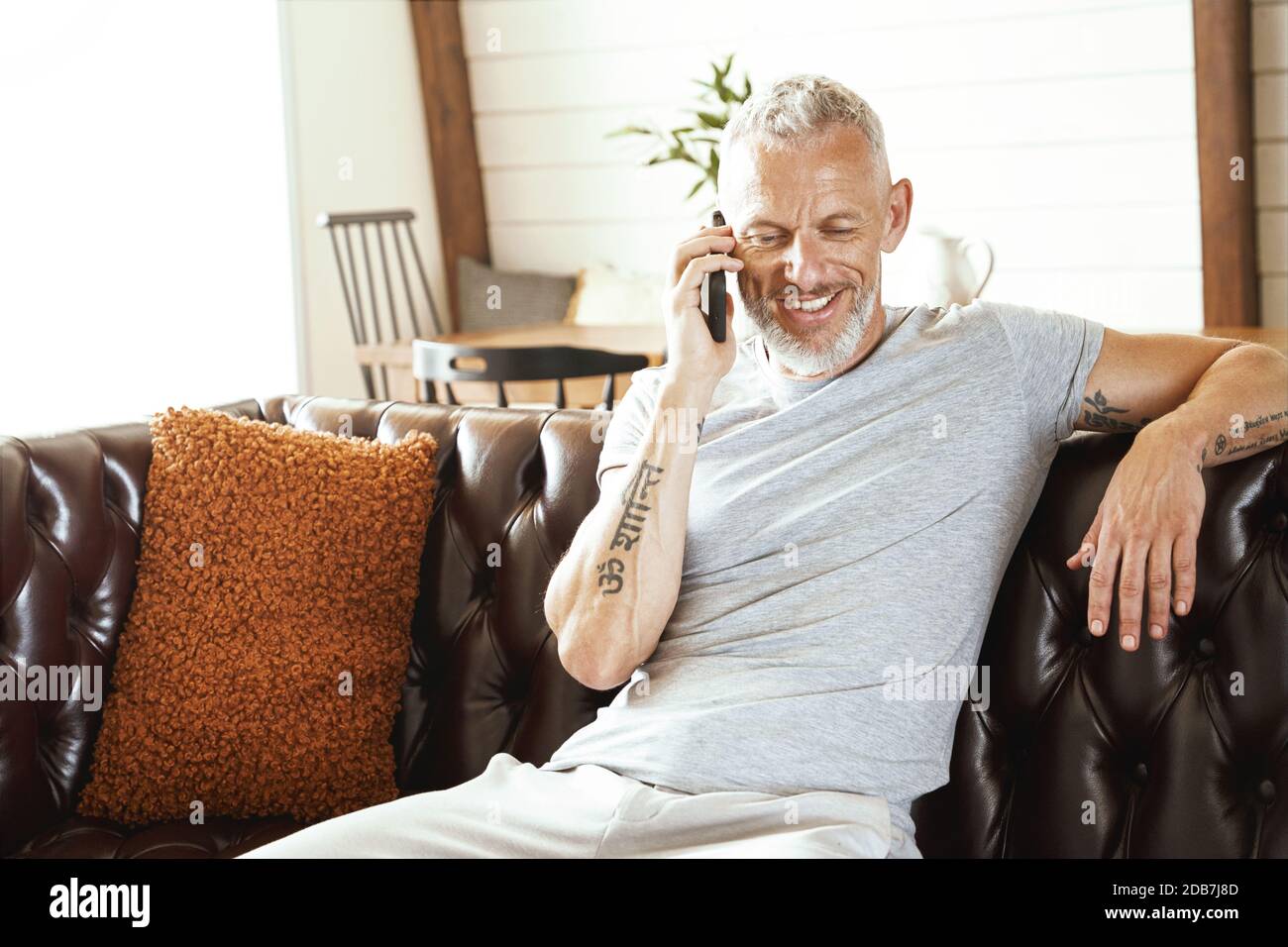 Glücklicher Kaukasischer Mann mittleren Alters, der mit Handy und sprach Lächelnd auf dem Sofa sitzen und von zu Hause aus arbeiten Stockfoto