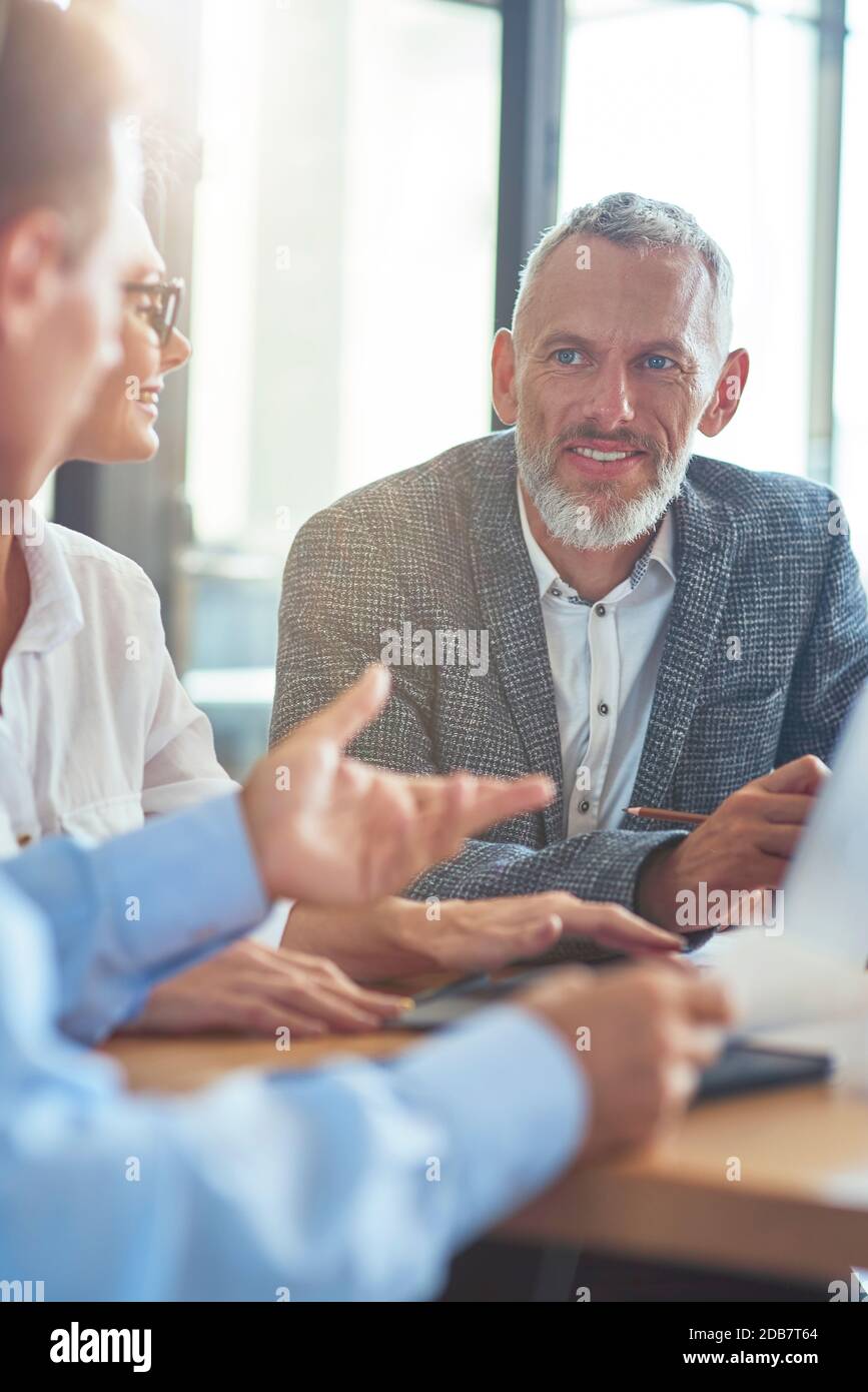 Fröhlicher reifer Geschäftsmann sitzt mit Kollegen im modernen Büro Und etwas zu diskutieren Stockfoto