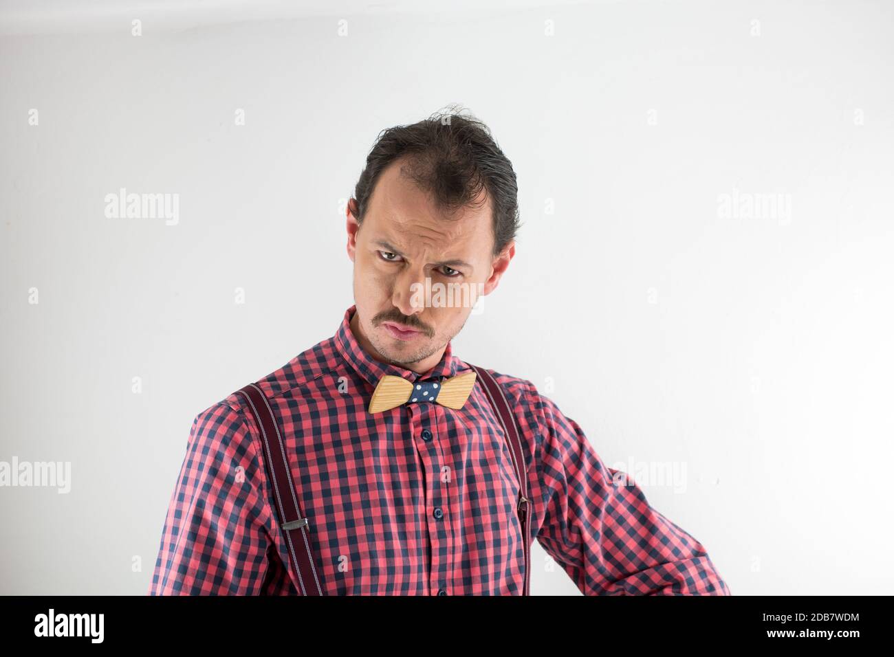 Studio-Porträt eines Mannes mit Holzbowtie, Hosenträger und Hemd. Dreißig Jahre alter Mann mit Schnurrbart, der die Kamera anschaut und Geste macht. Stockfoto