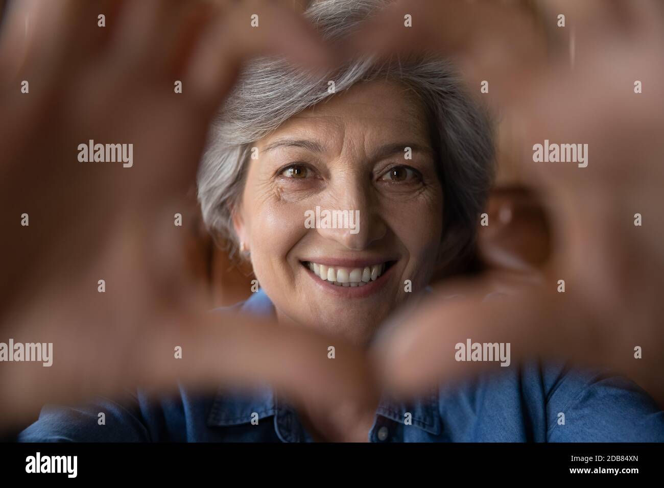 Nahaufnahme lächelnd reife grauhaarige Frau zeigt Herz-Geste Stockfoto