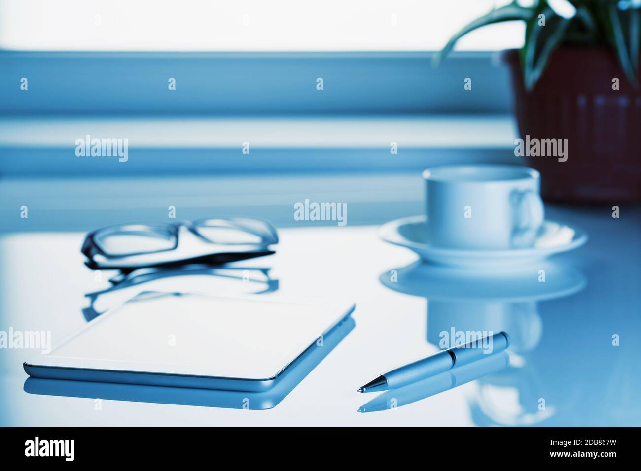 Tablet-Computer, Brille und eine Tasse auf dem Tisch in einem blauen getönt. Entfernte Logos, Tasten, ändern Sie die ursprüngliche Größe. Stockfoto