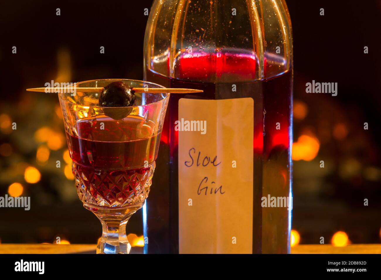 Flasche und Glas selbstgemachten Schlehen Gin. Mit einer Schlehbeere auf dem Glas. Stockfoto