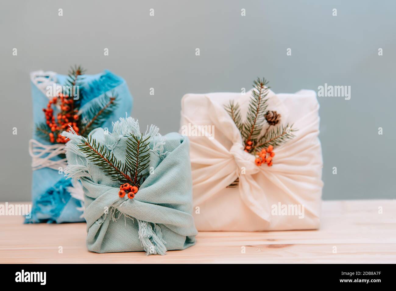 Zero Waste weihnachtskonzept. Geschenkschachteln in Stoff mit Fichtenzweig und Beeren auf Holzhintergrund eingewickelt. Flatlay. Umweltfreundlich nachhaltig Stockfoto