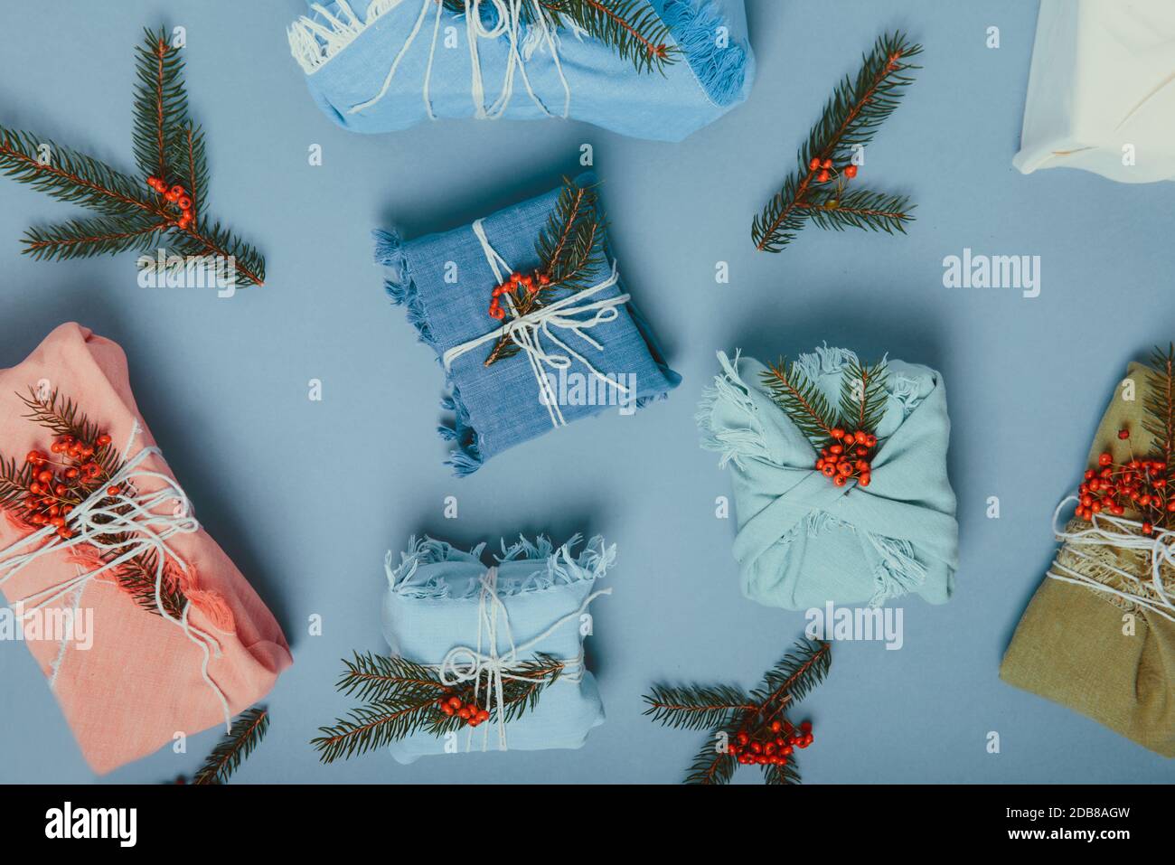 Draufsicht Zero Waste weihnachtskonzept. Geschenkschachteln in Stoff mit Fichtenzweig und Beeren auf gedämpftem blauen Hintergrund gewickelt. Flatlay. Umweltfreundlich Stockfoto